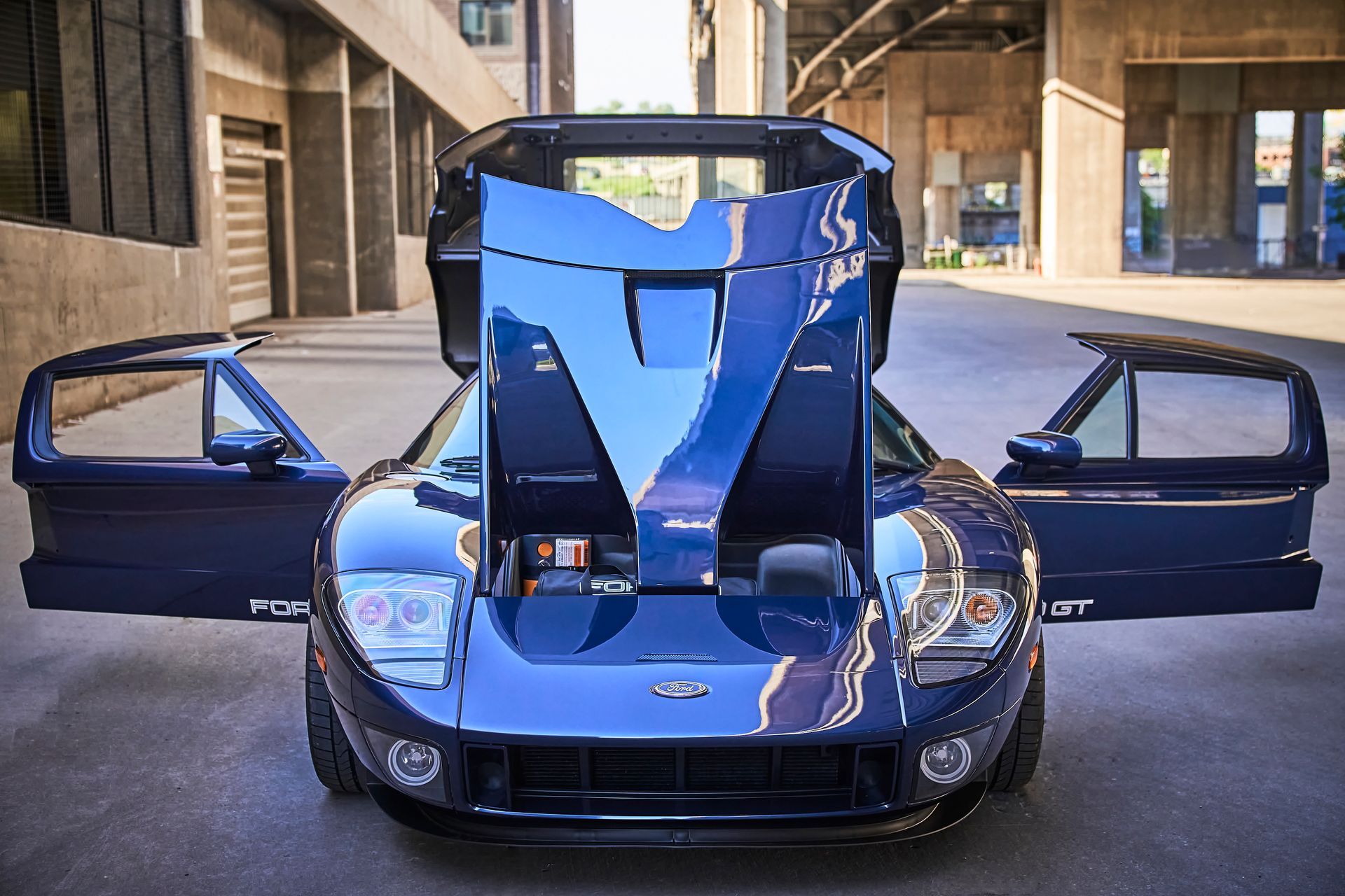 A blue sports car with its hood up and its doors open