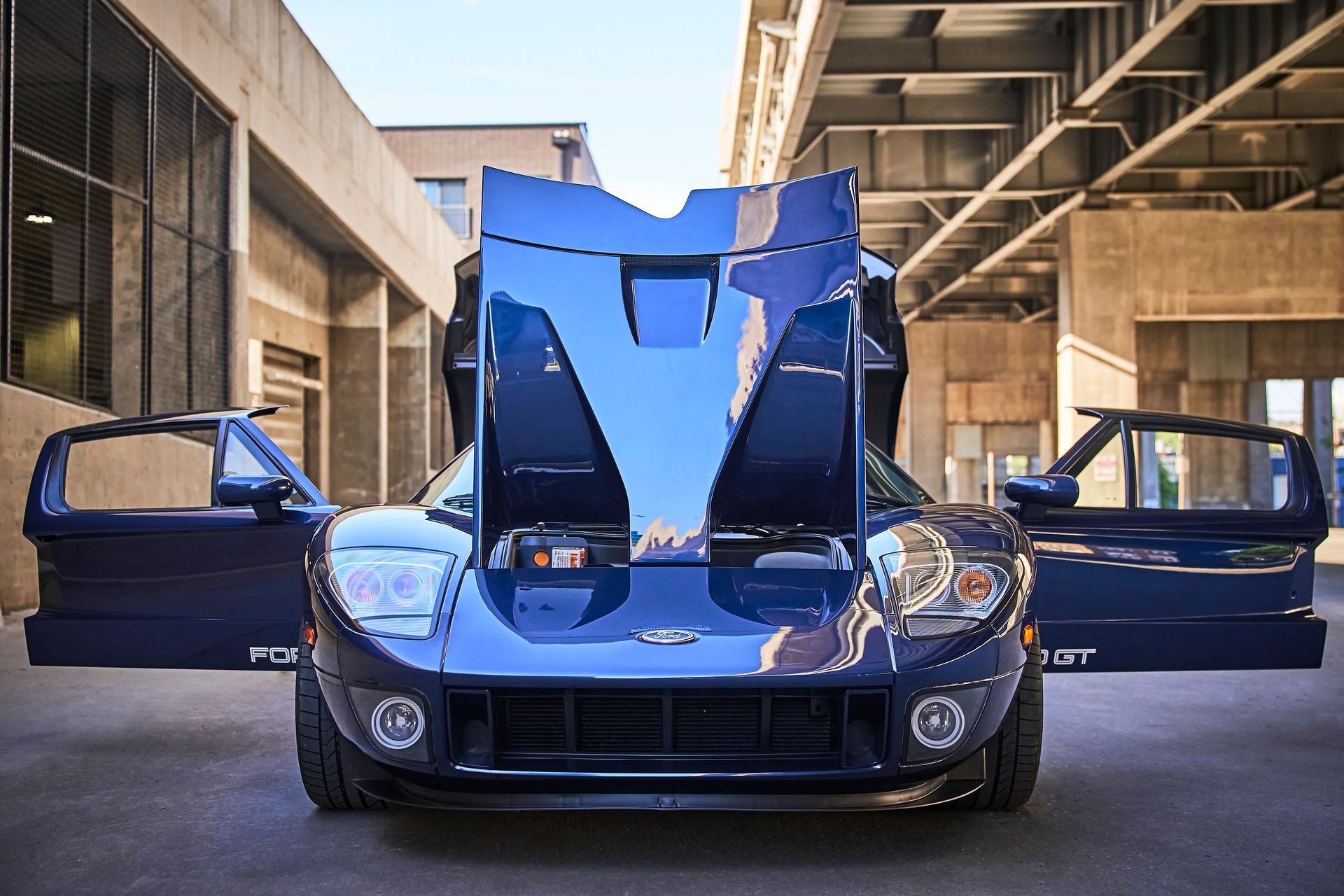 A blue sports car with its hood open is parked in a parking lot.