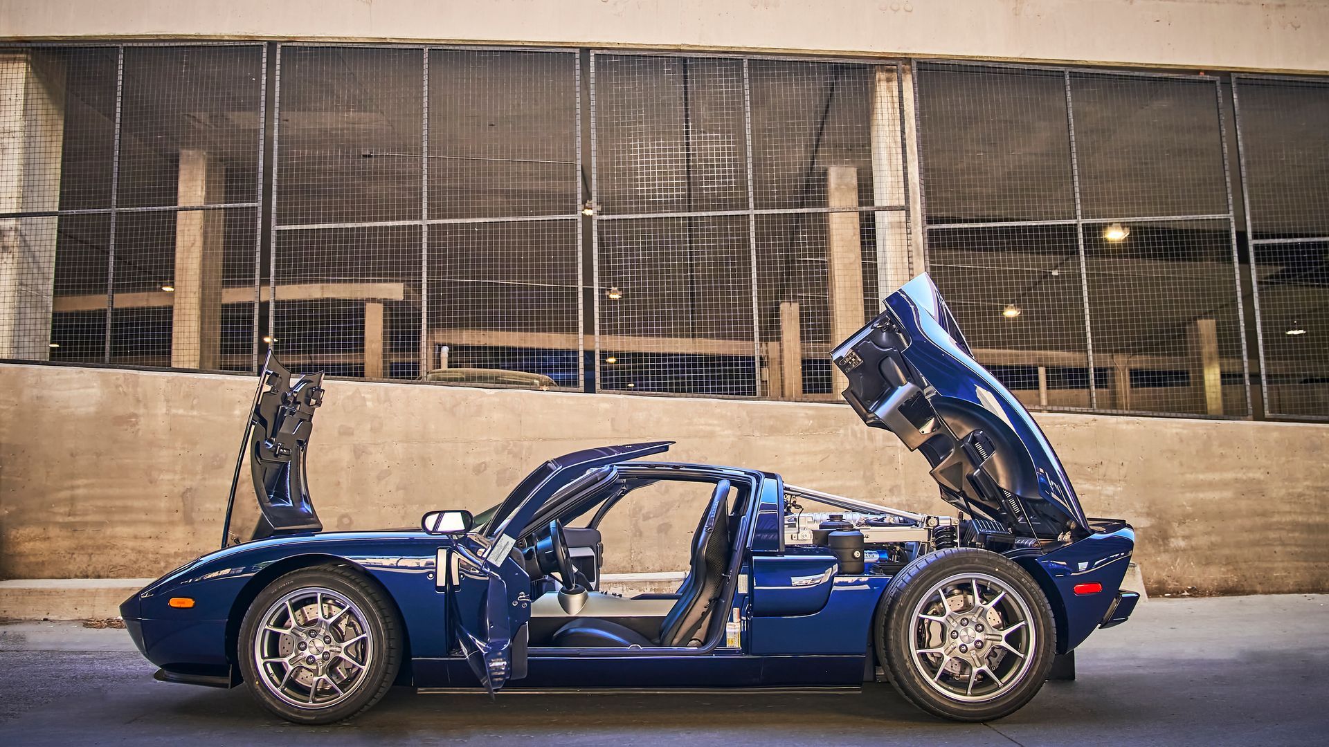 A blue sports car with the hood up is parked in front of a building.