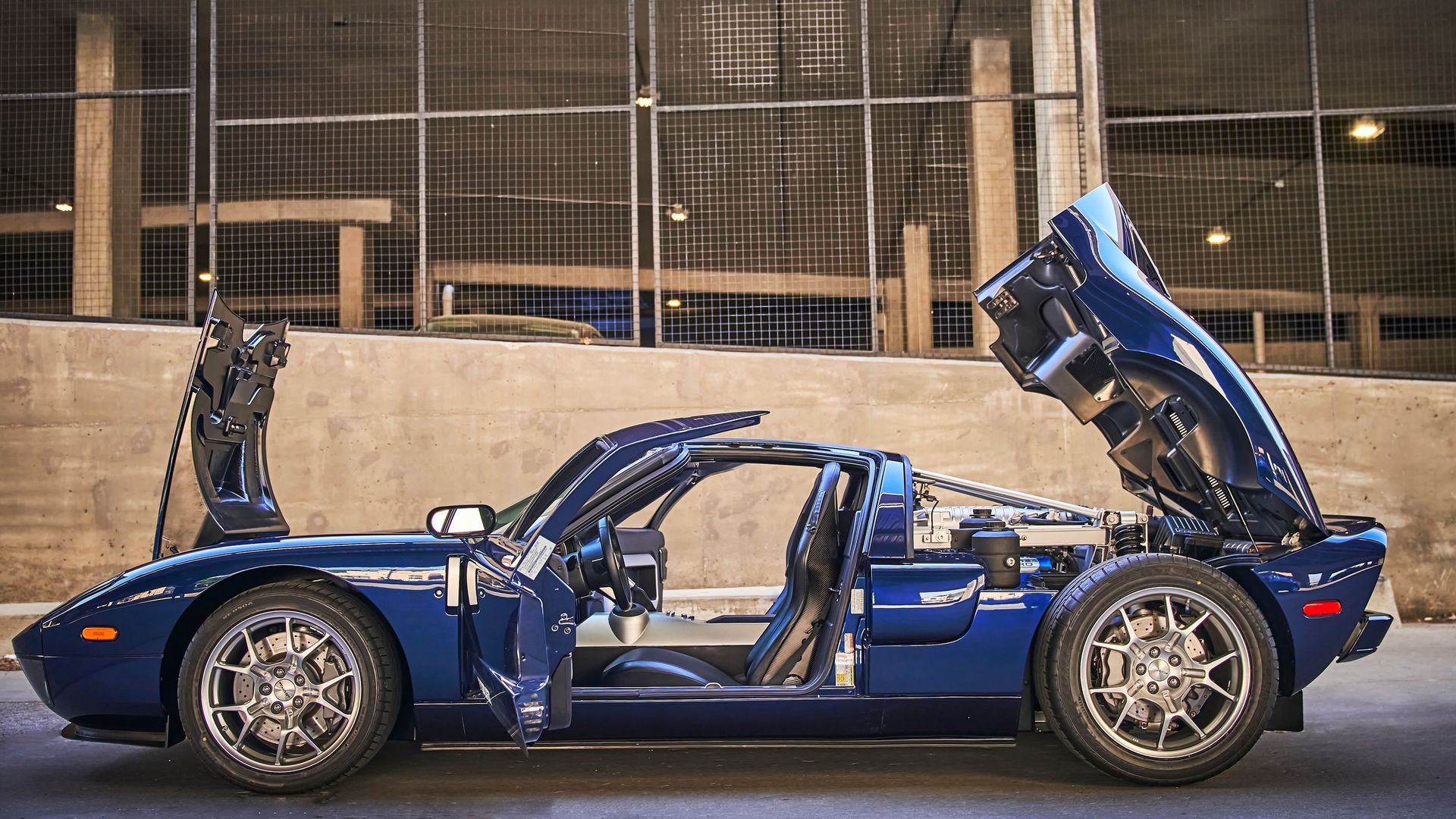 A blue sports car with the hood up is parked in front of a building.