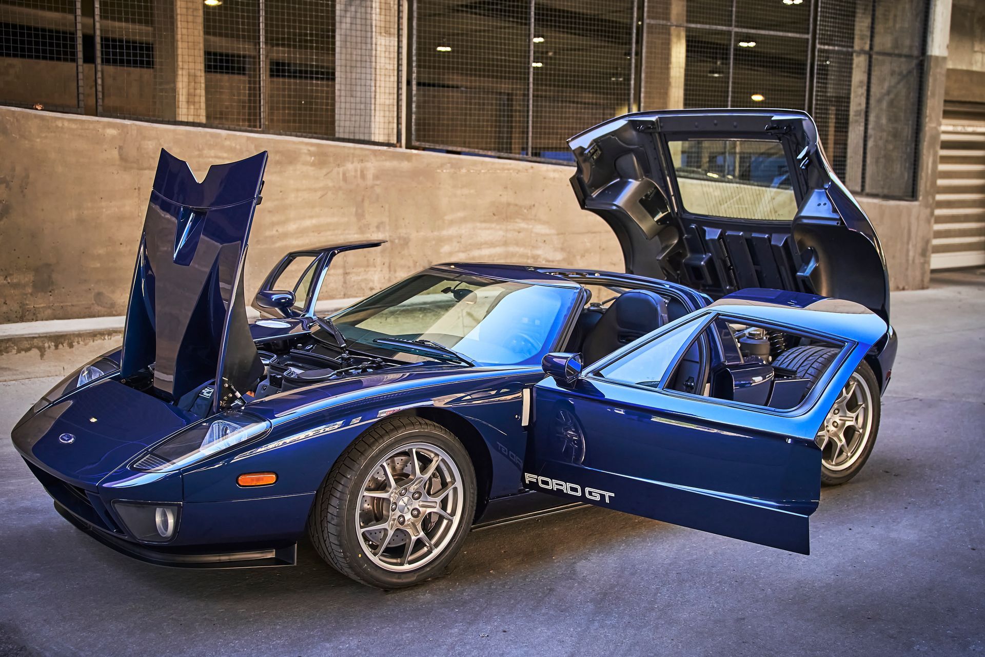A blue sports car with its hood open is parked in a parking lot.