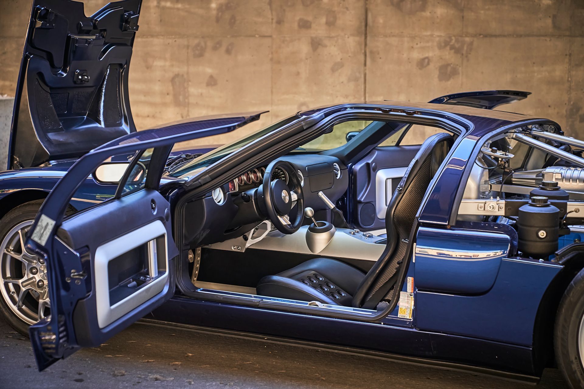 A blue sports car with its doors open is parked in front of a wall.