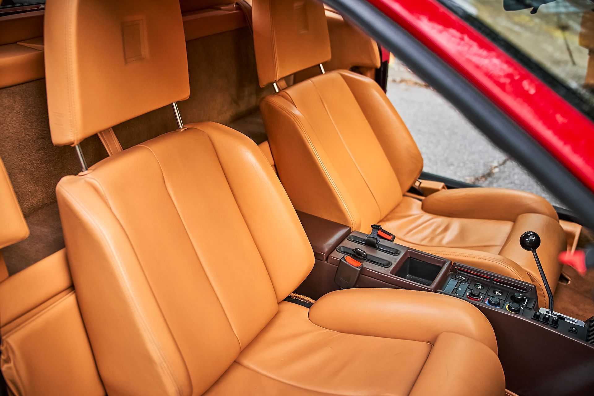The interior of a red car with brown leather seats.