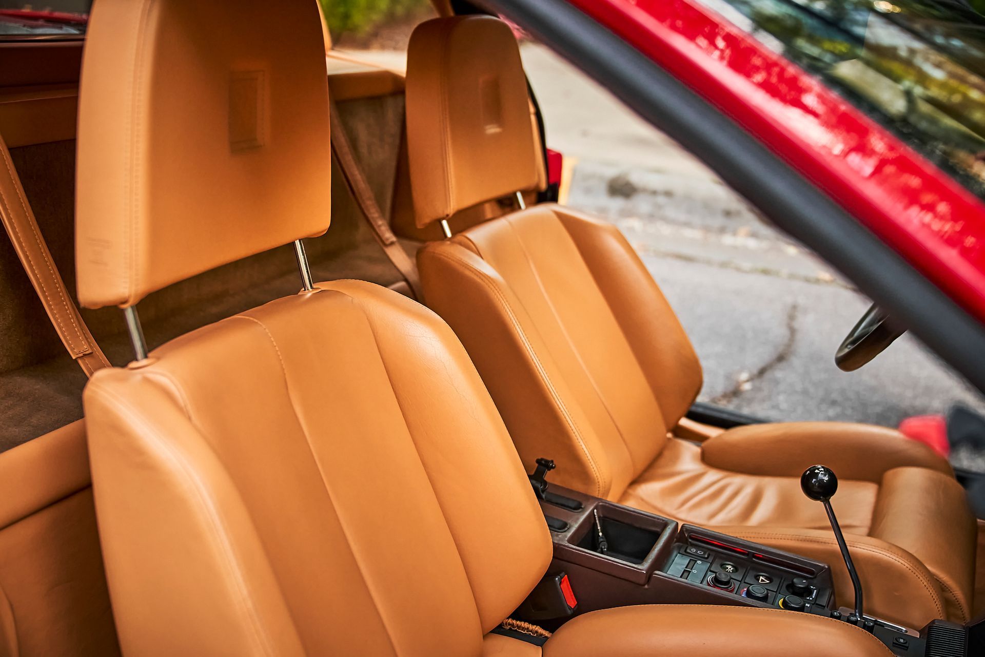 The interior of a red car with brown leather seats.