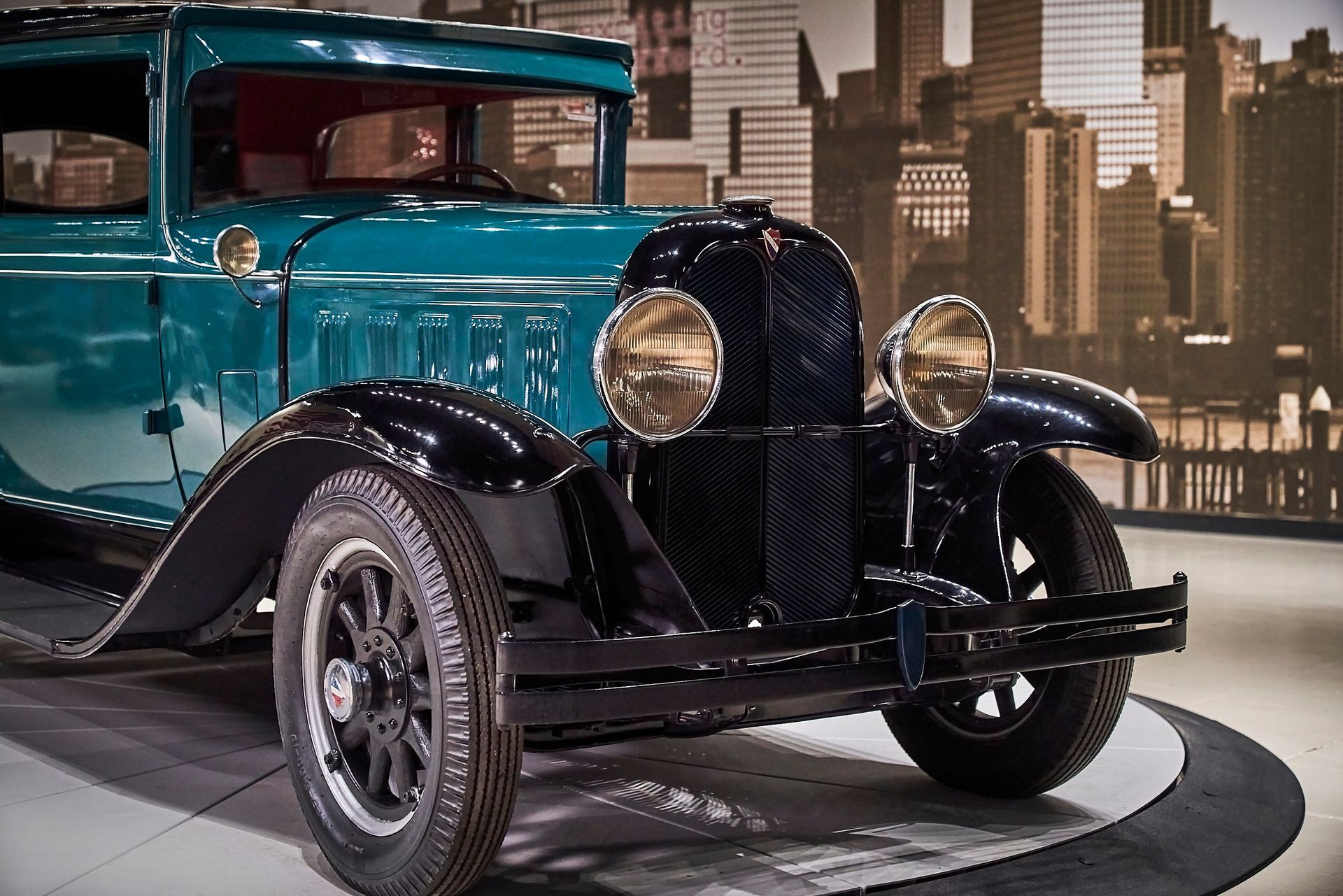 An old car is parked in front of a city skyline