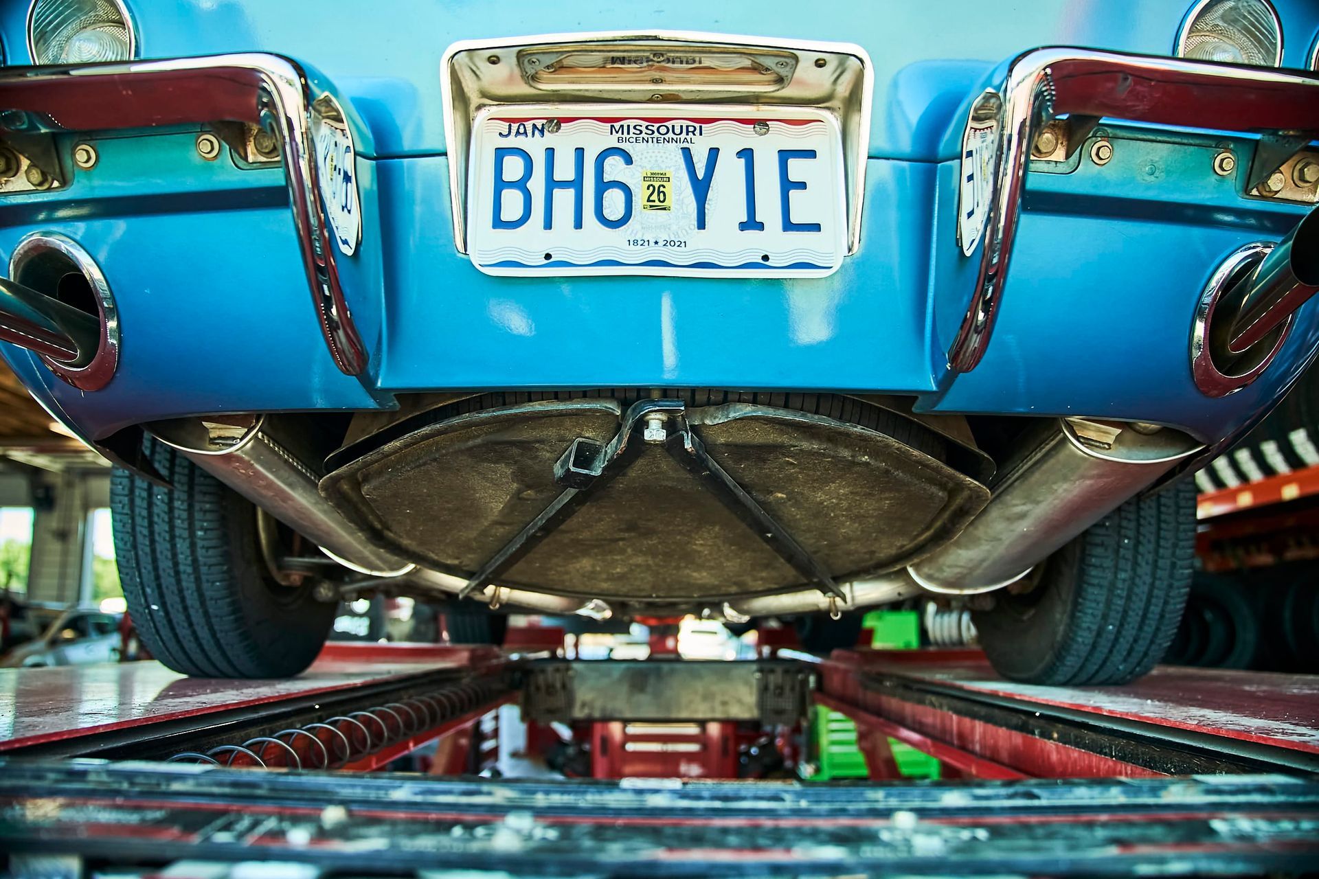 Blue classic car's underside on a lift, showing exhaust pipes, license plate 