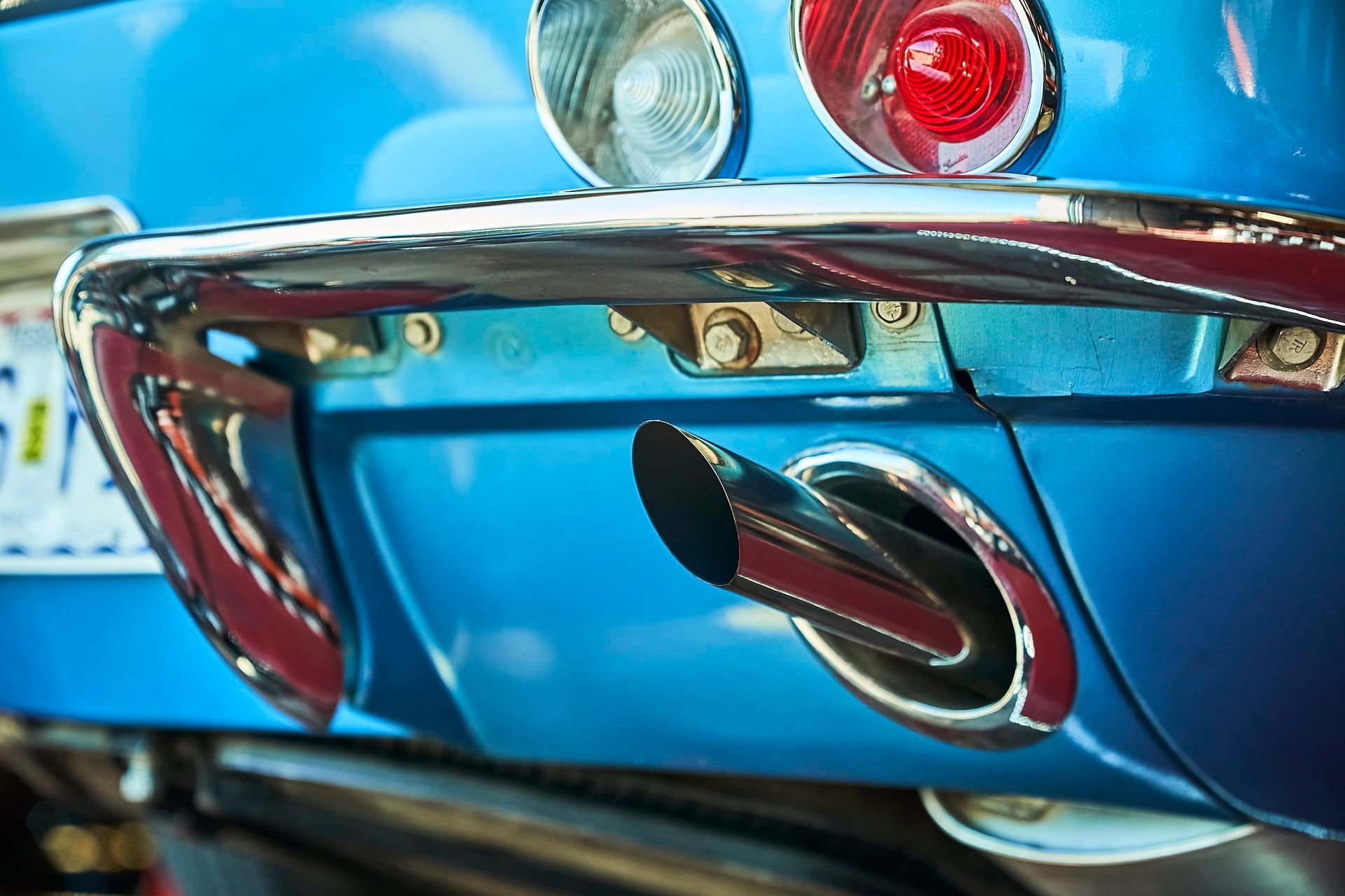 Close-up of a classic blue car's rear end, showing the exhaust pipe, chrome bumper, and red taillight.