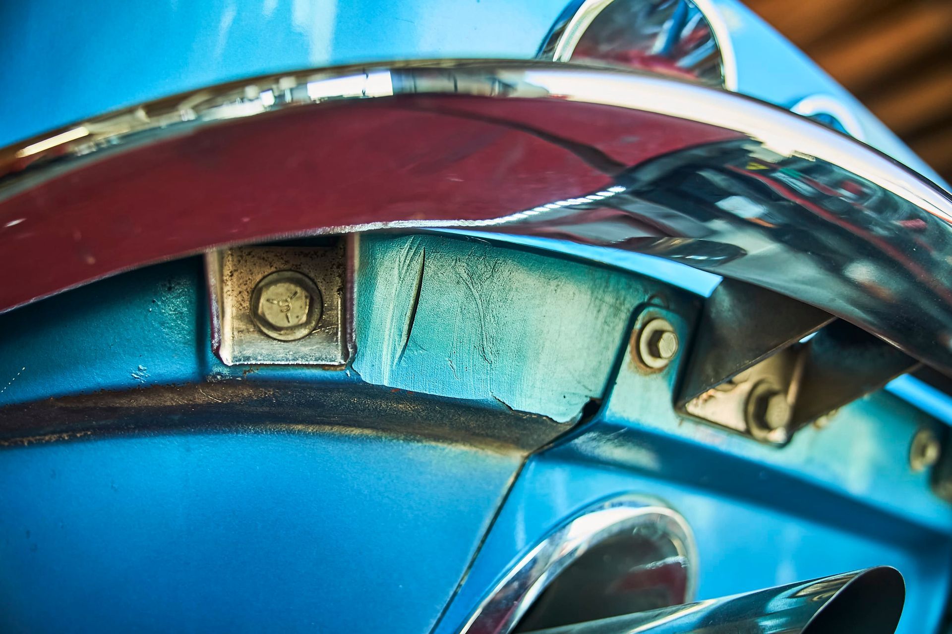 Close-up of a vintage blue car's bumper and trim with chrome accents and visible wear.