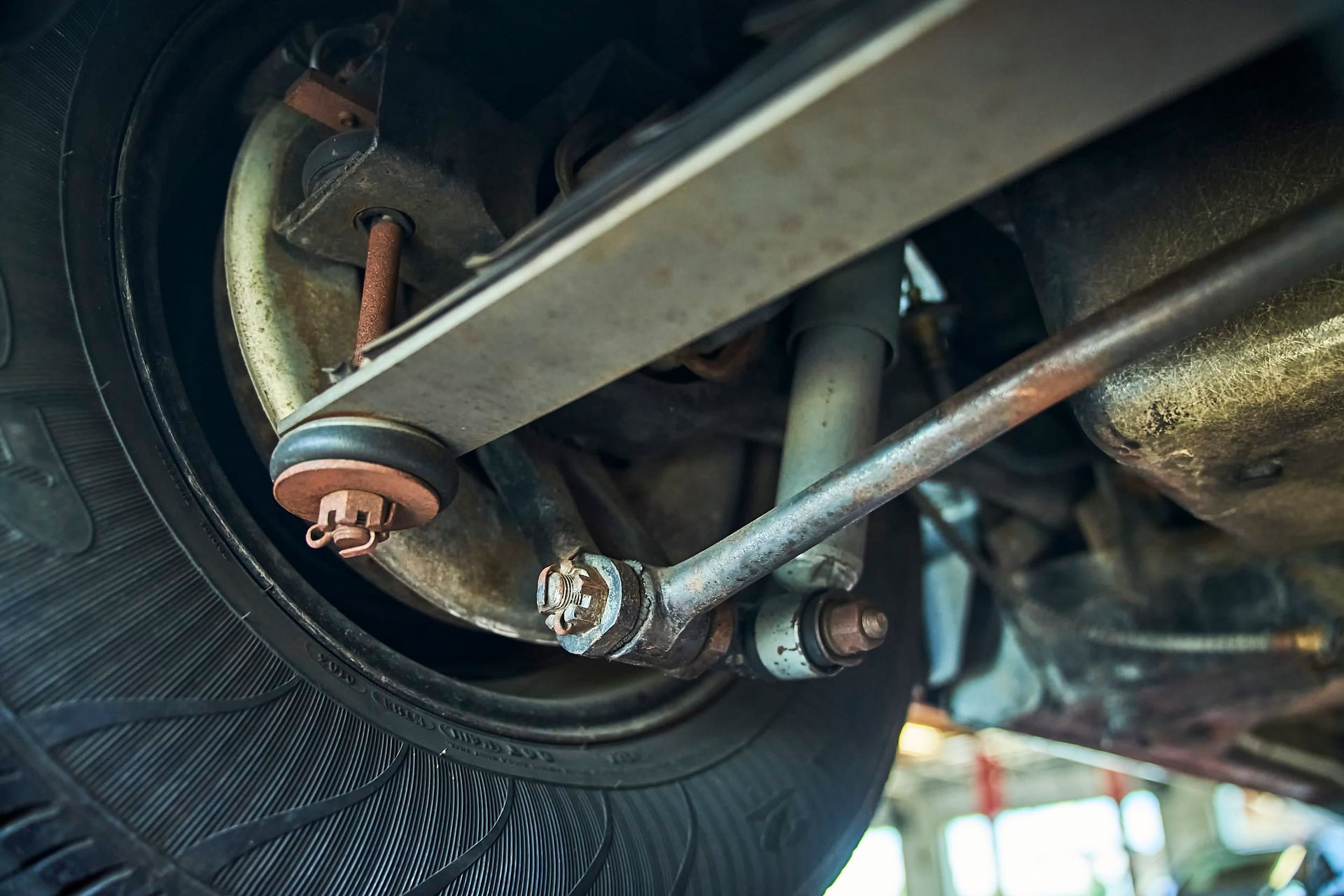 Undercarriage of a vehicle, showing the suspension system with a rusty tie rod, wheel, and shock absorber.