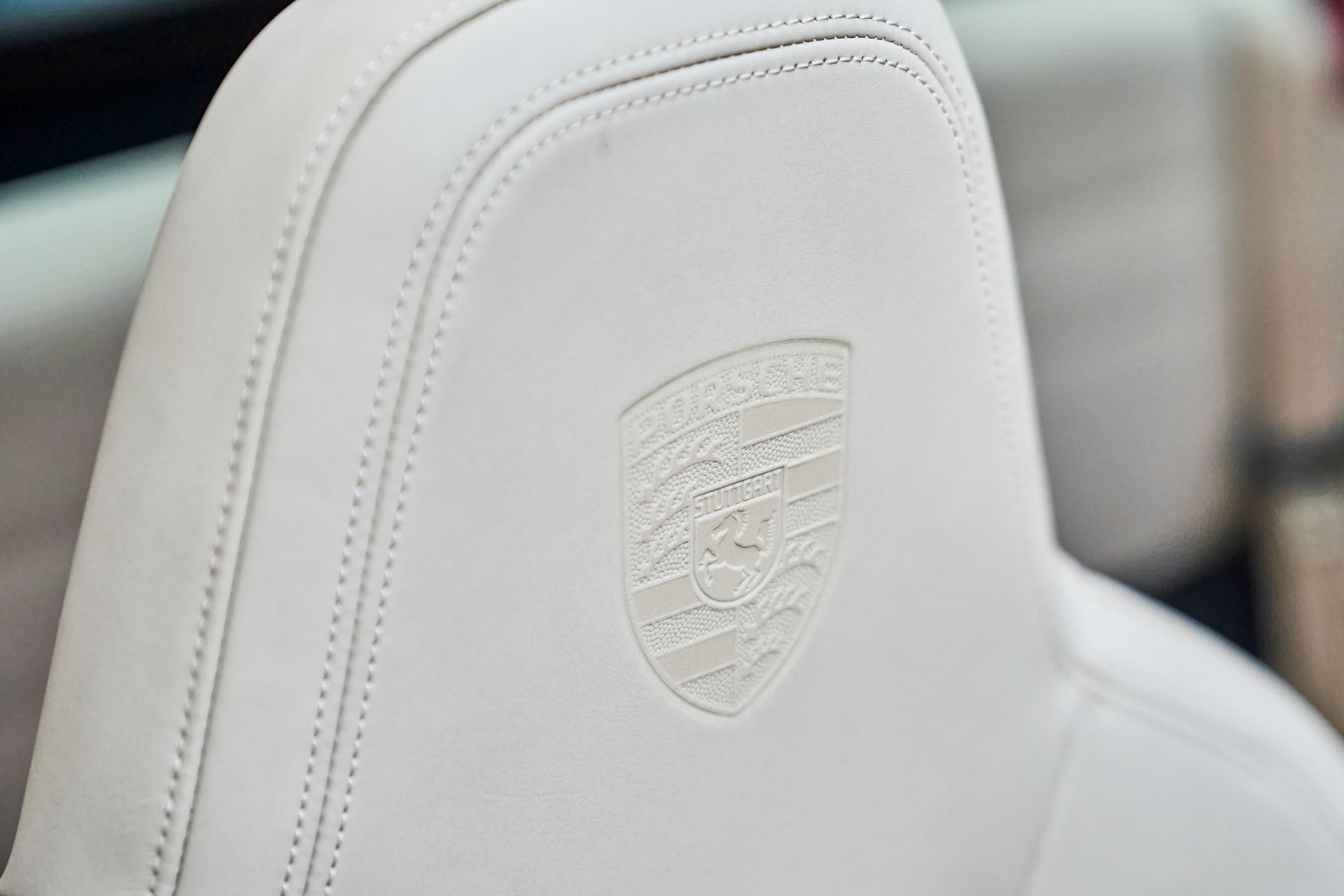 A close up of a white leather seat with a porsche logo on it.