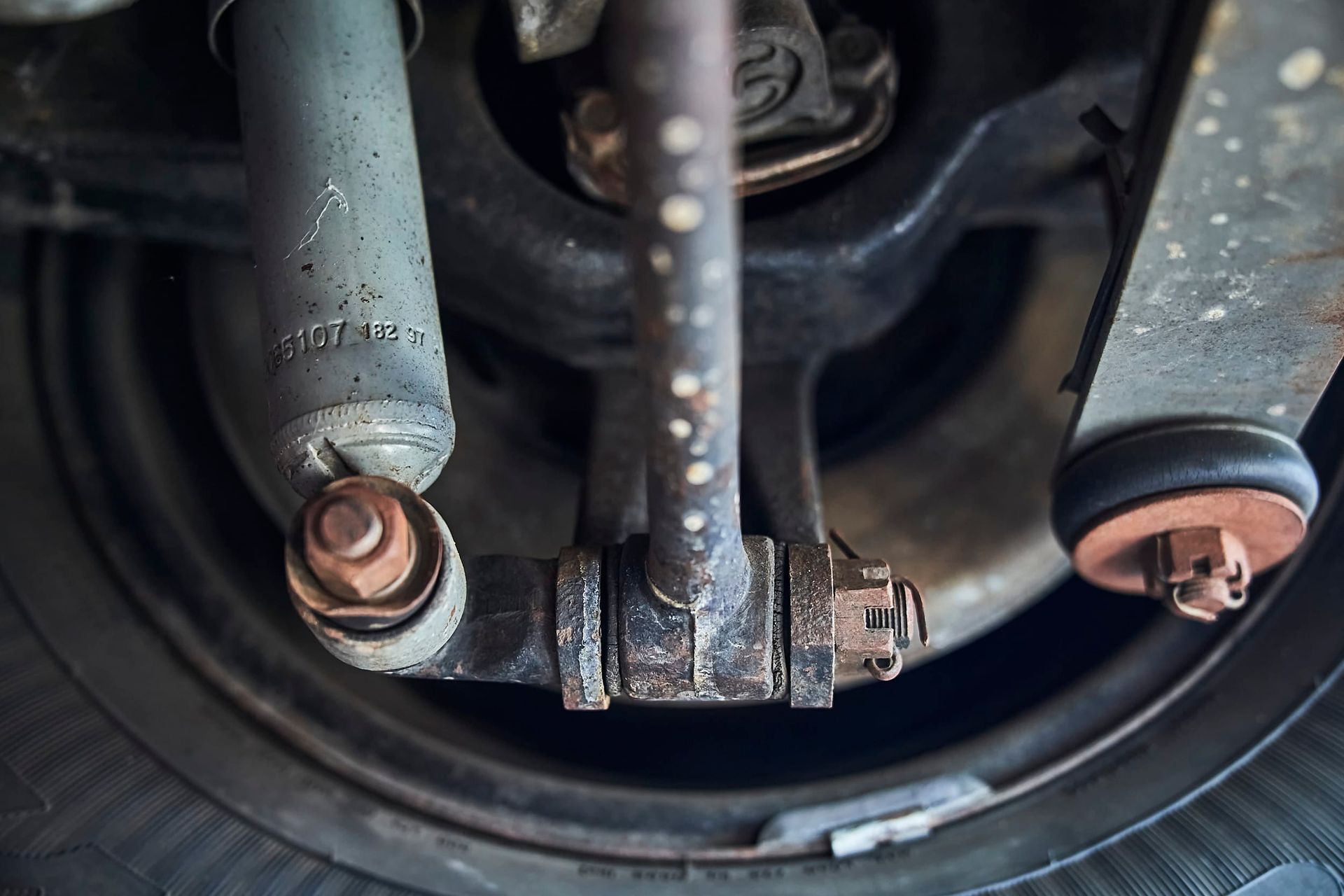 Close-up of car suspension components: shock absorber, sway bar link, and wheel. Rusty, metallic colors.