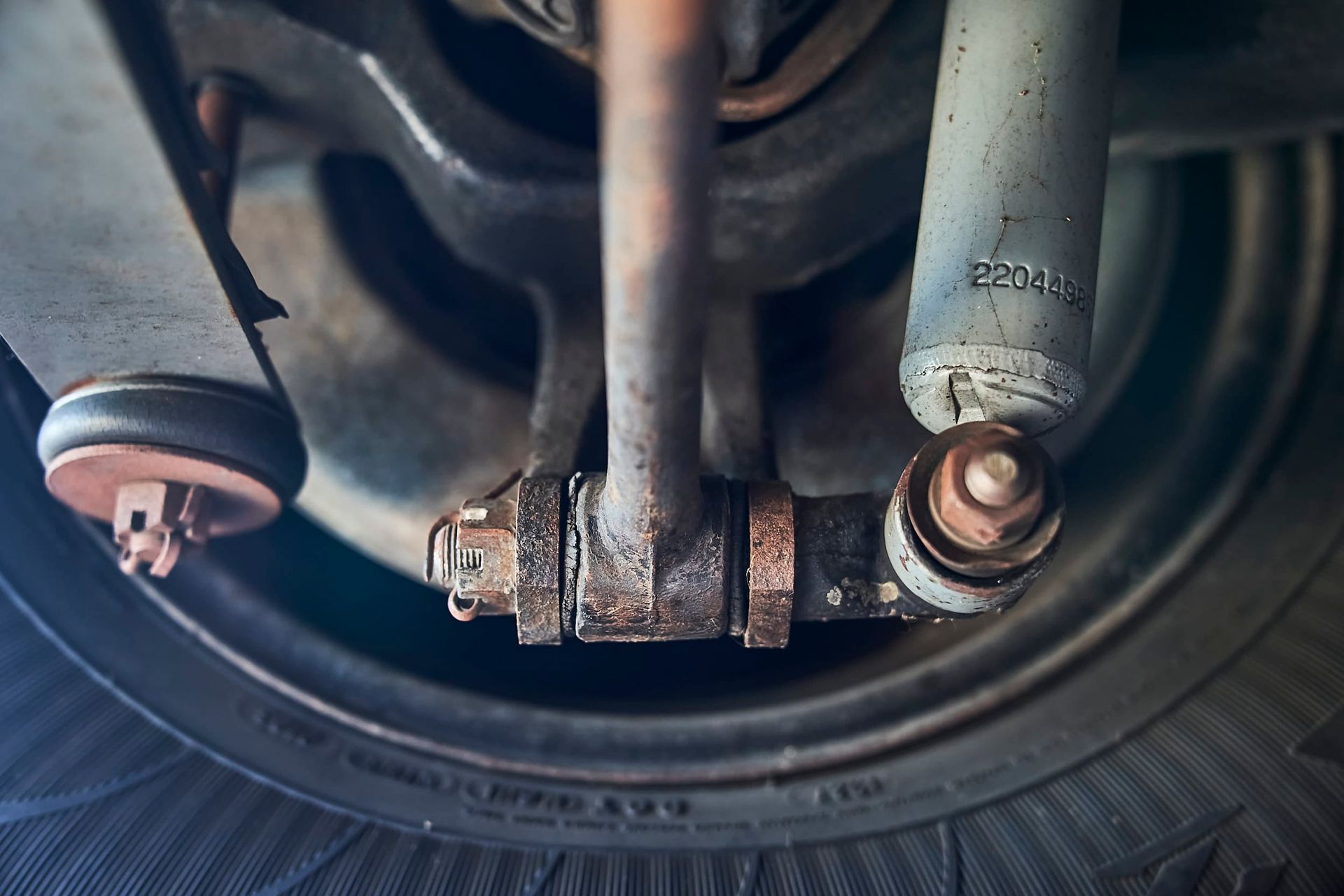 Close-up of a vehicle's rusty suspension components, including a shock absorber, tire, and various metal parts.