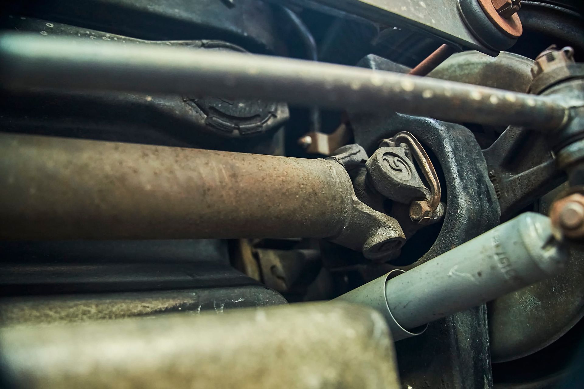 Close-up view of a rusty car driveshaft, showing a U-joint and surrounding components.  The shot is from underneath the vehicle.