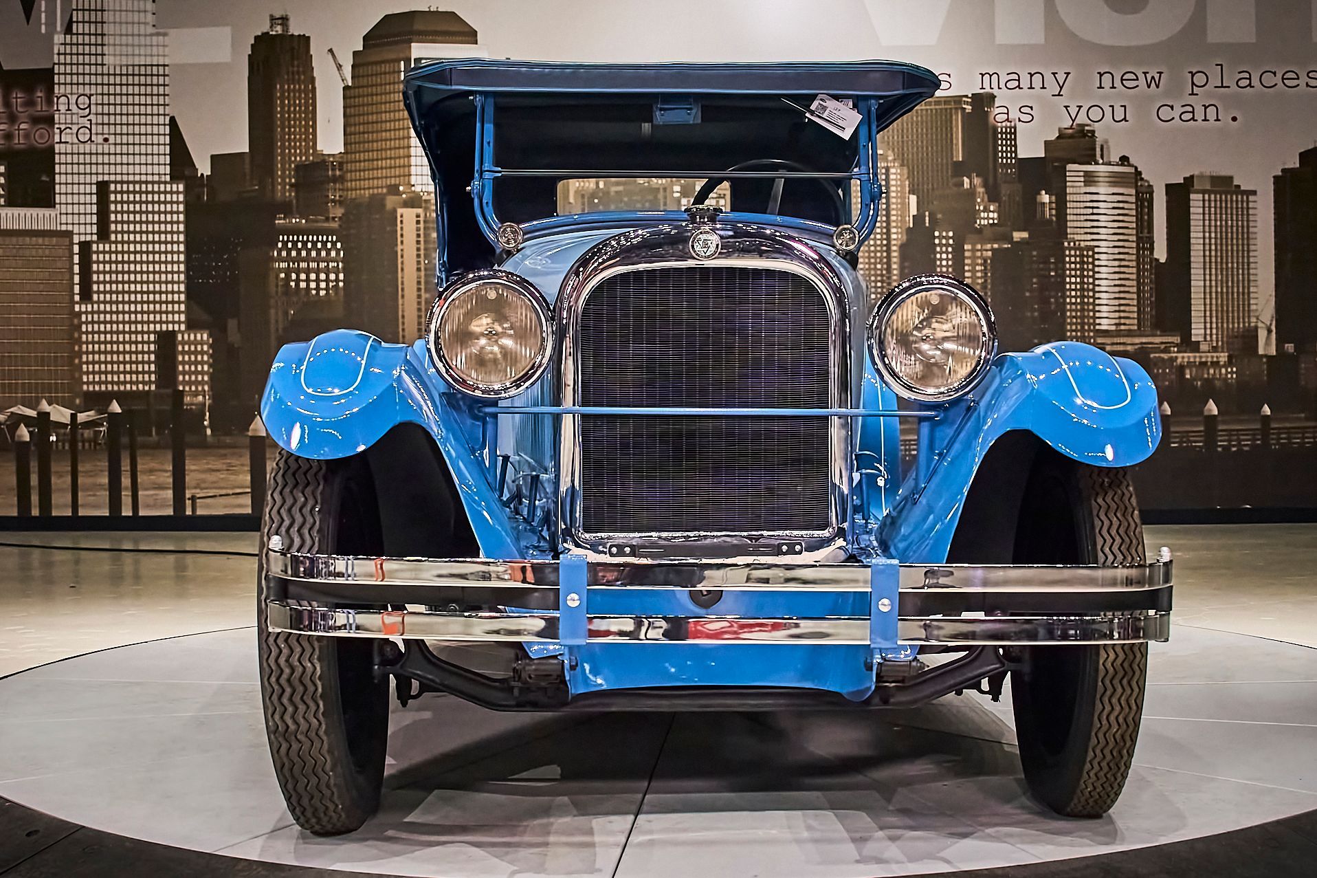 An old blue car is parked in front of a city skyline