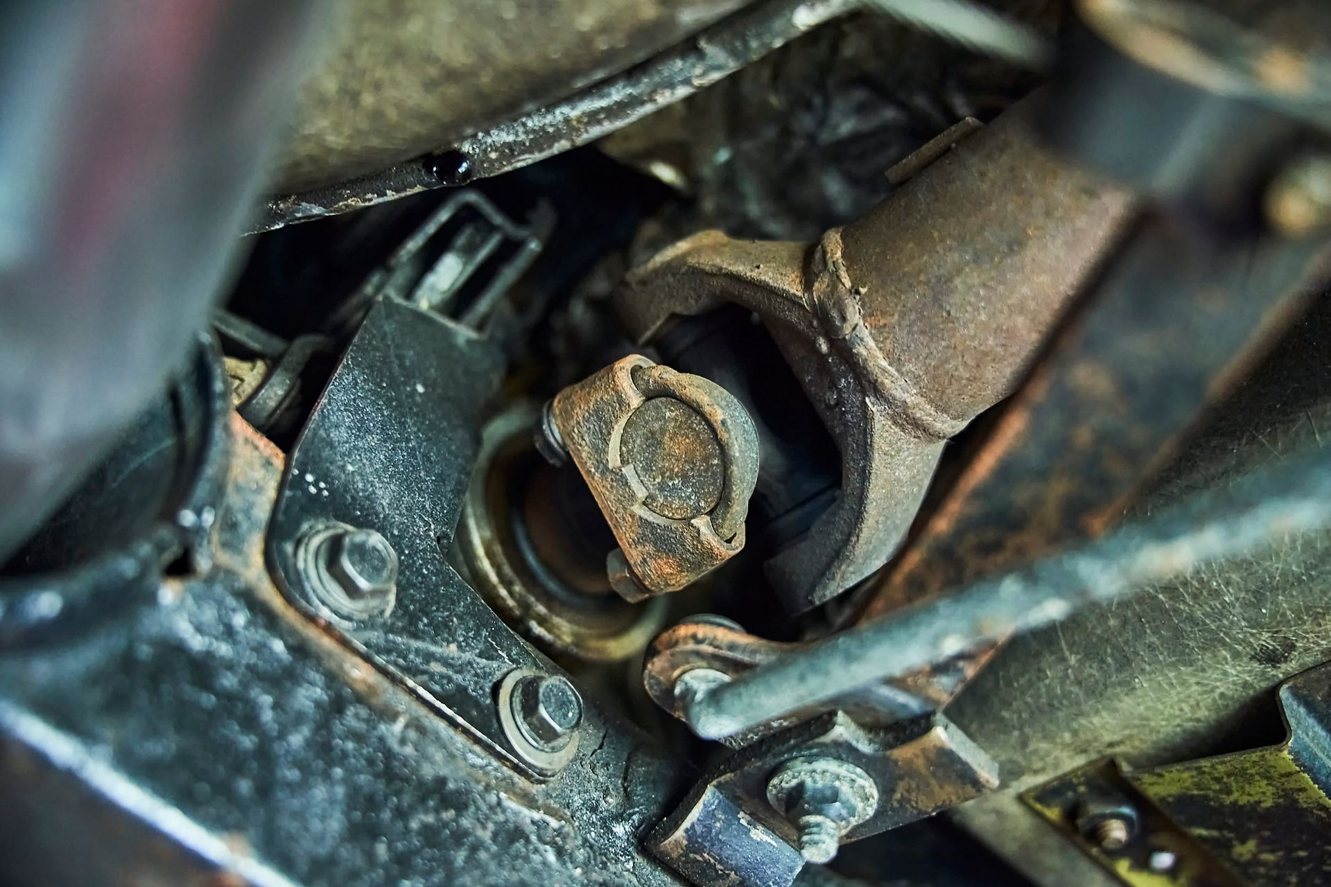 Close-up of a rusty vehicle driveshaft joint with bolts and surrounding metal components.