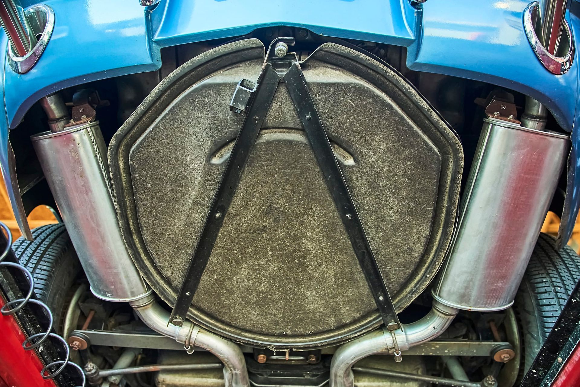 Undercarriage of a blue classic car, showing exhaust pipes, a central panel, and suspension details.