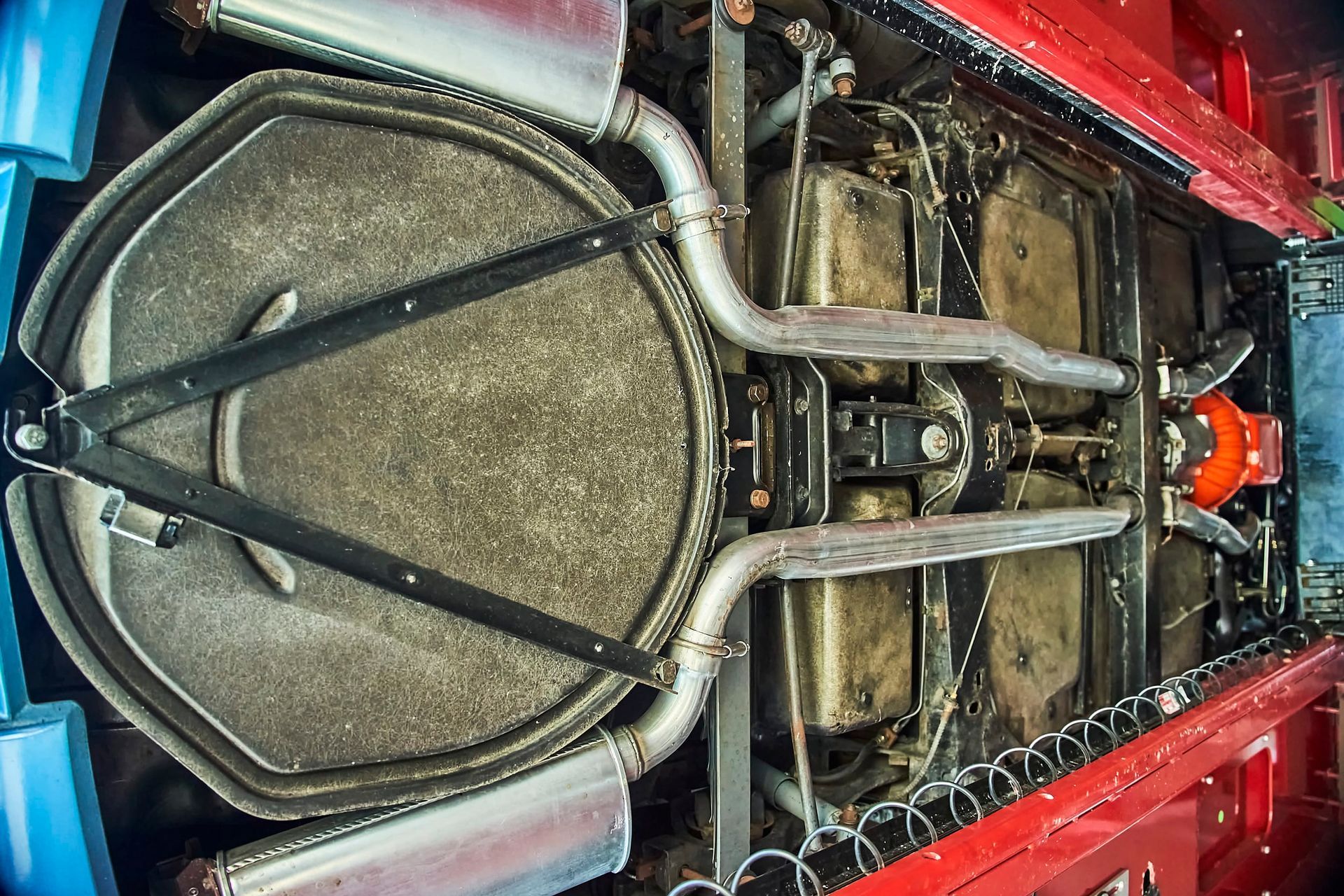 Underside of a red car, showing exhaust system and drivetrain. A large circular structure dominates the center.