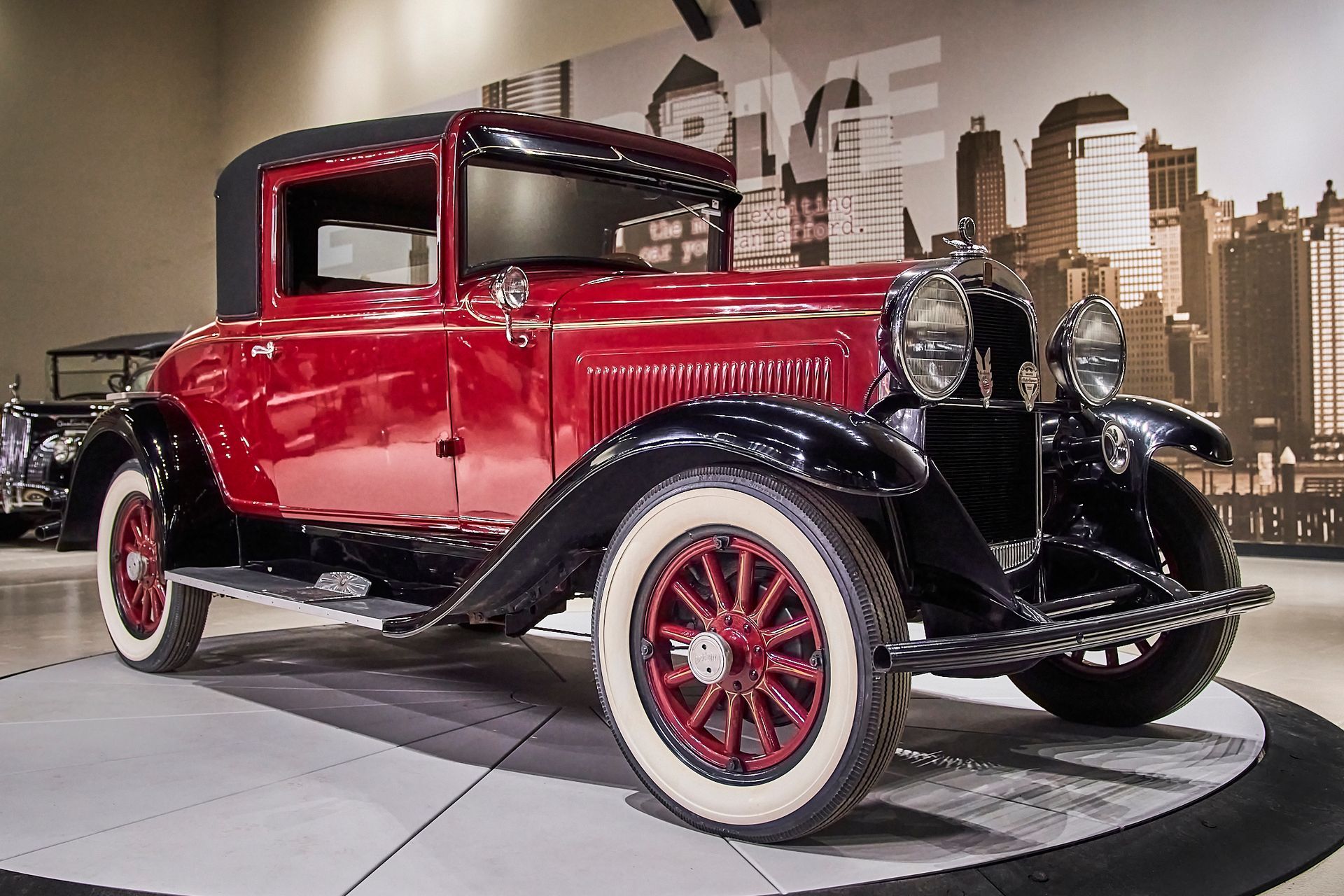An old red car with white tires is on display