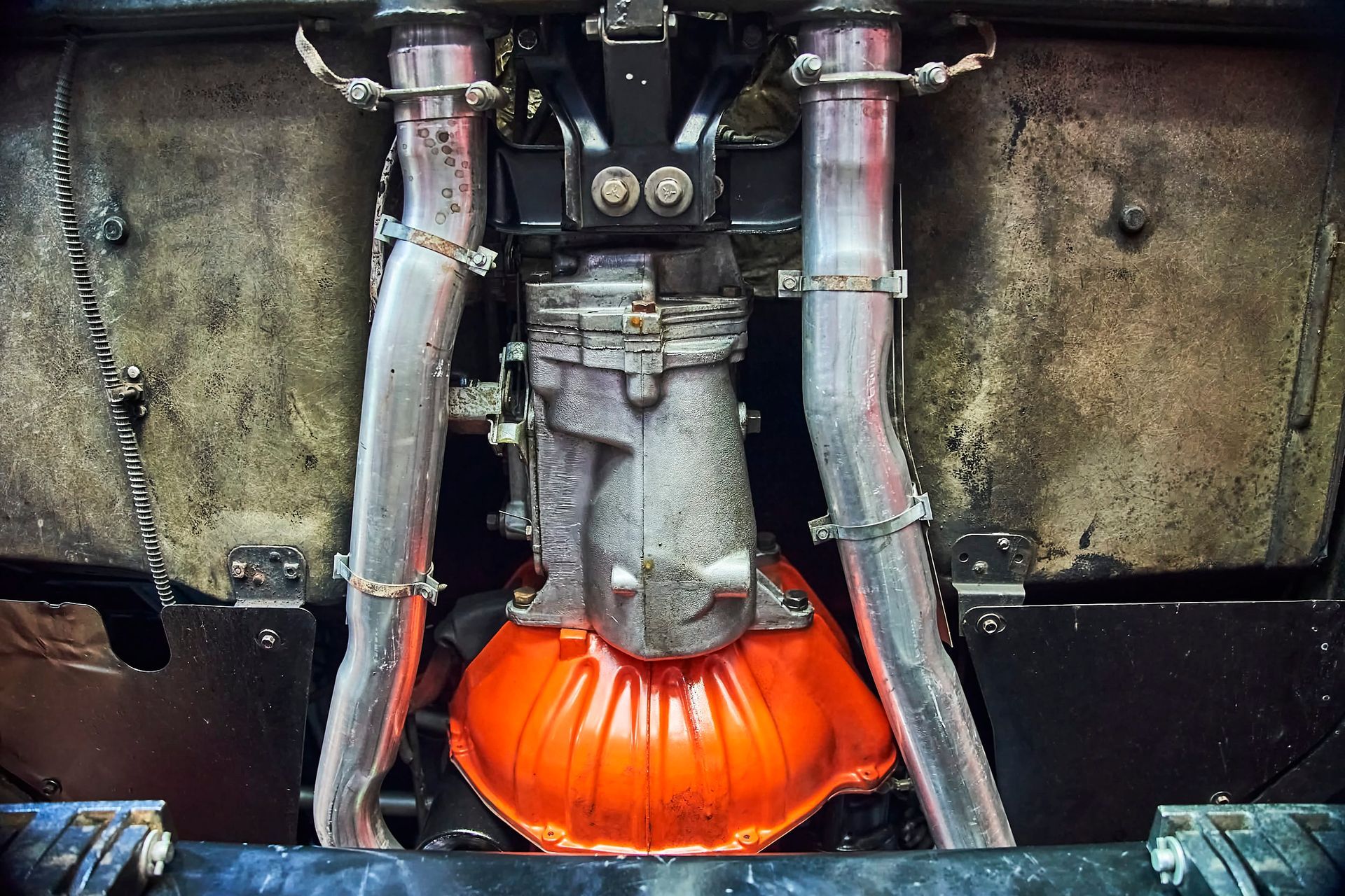 Undercarriage of a vehicle: a transmission and exhaust pipes are visible. The transmission has an orange covering.