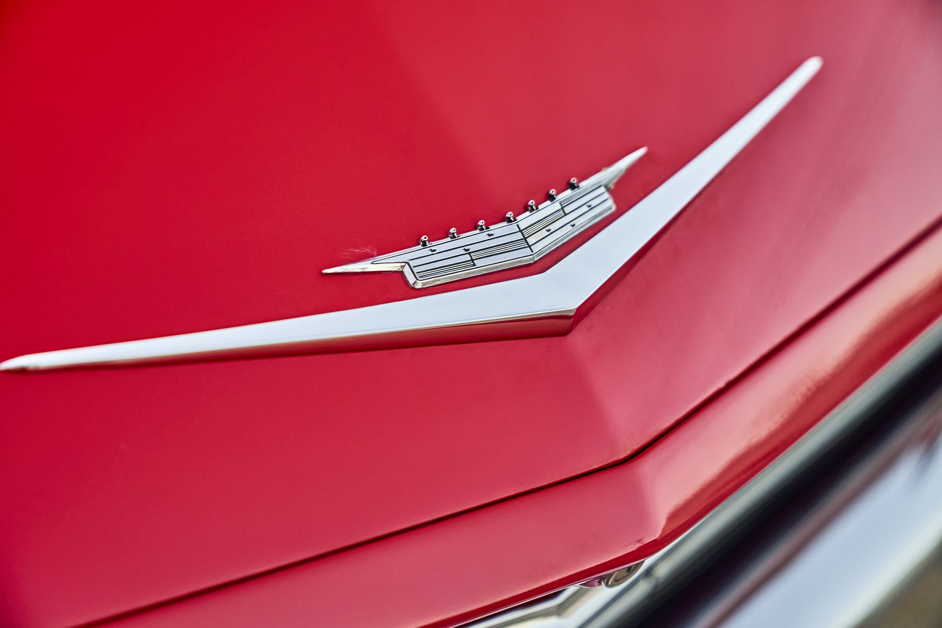 The hood of a red car with a silver emblem on it.