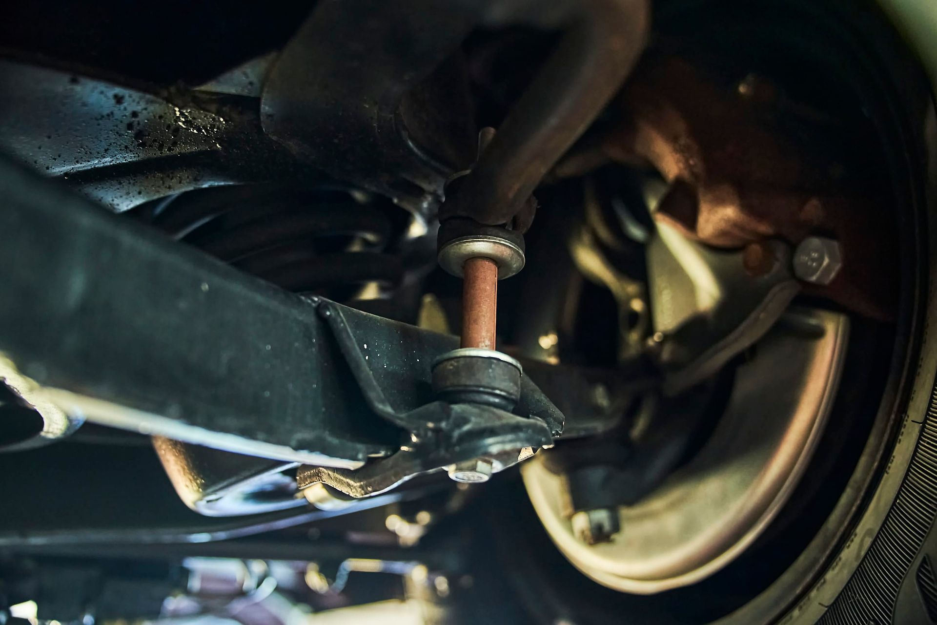 Underside view of a car's suspension with a rusty red connecting rod, black components, and a tire.