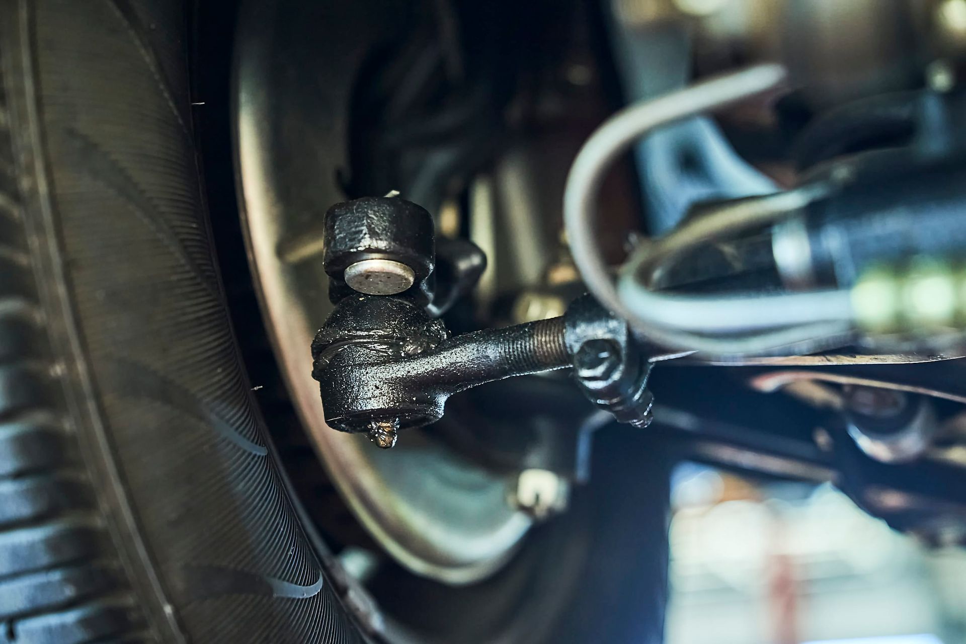 Close-up of a car's suspension component, likely a tie rod end, covered in grease near a tire.