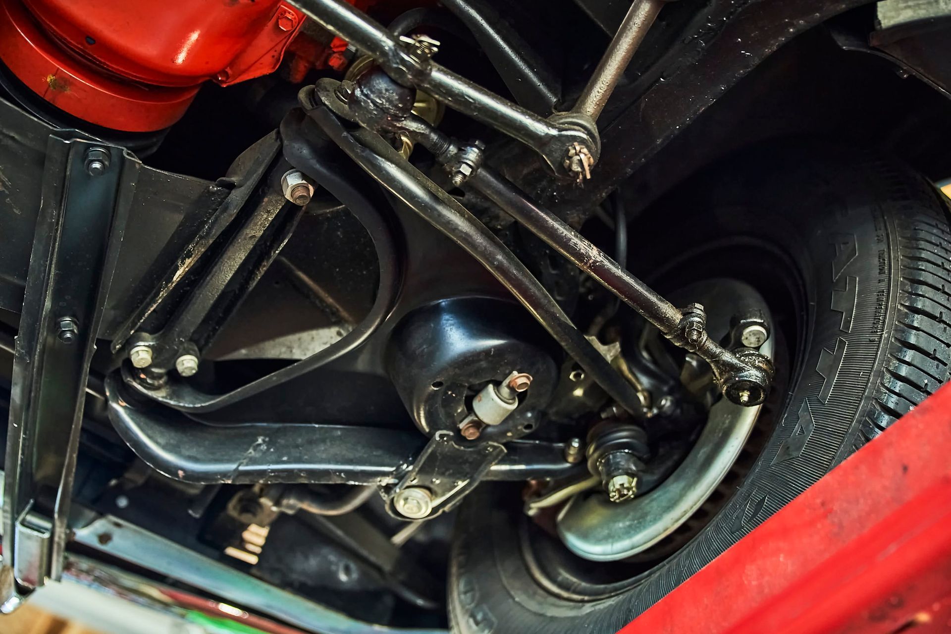 Black car suspension and steering components viewed from below. Includes tires, shocks, and various arms.