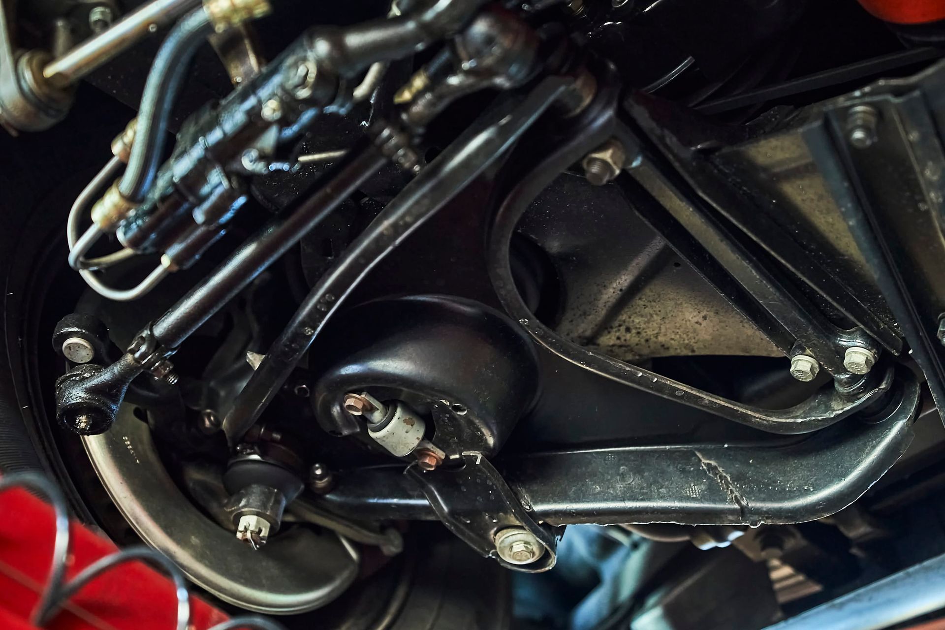 Black car suspension components, including control arms, steering linkage, and shock absorber, viewed from below.