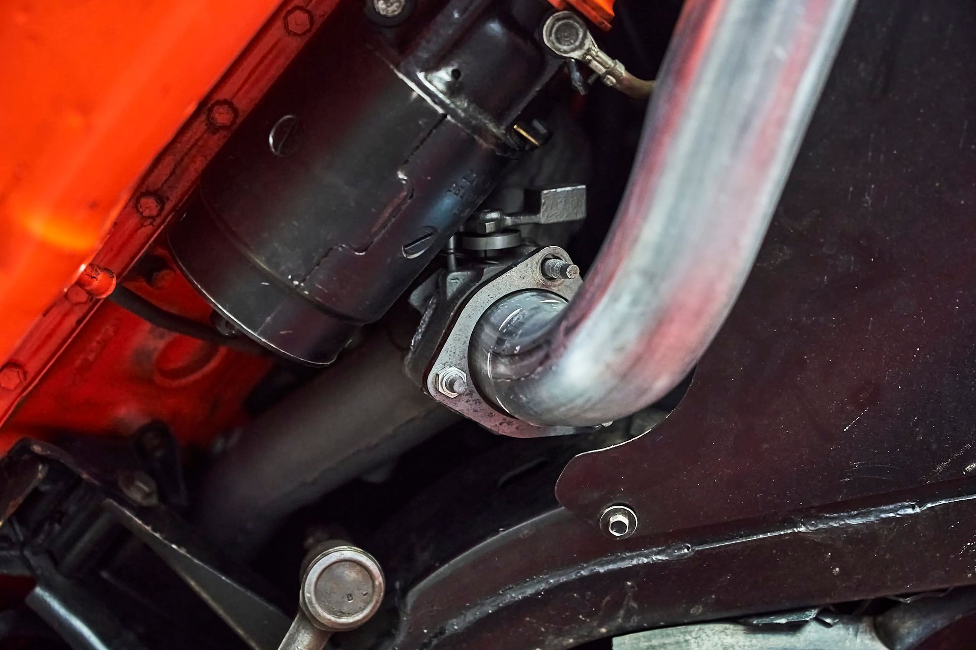 Close-up of car engine exhaust system, showing pipes connected to the engine block with metal flanges and bolts.