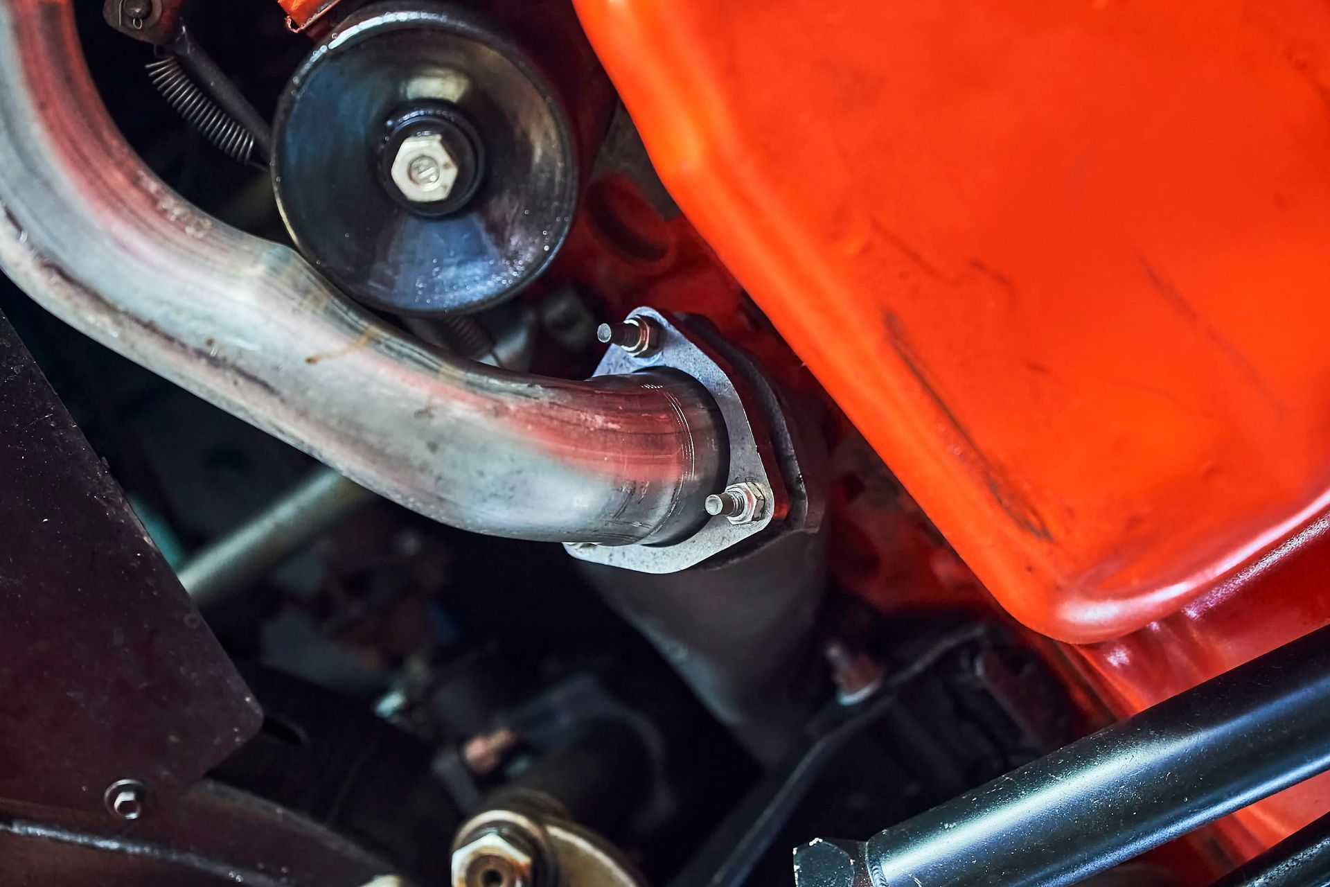 Close-up of a car engine component with silver exhaust pipe and orange block.