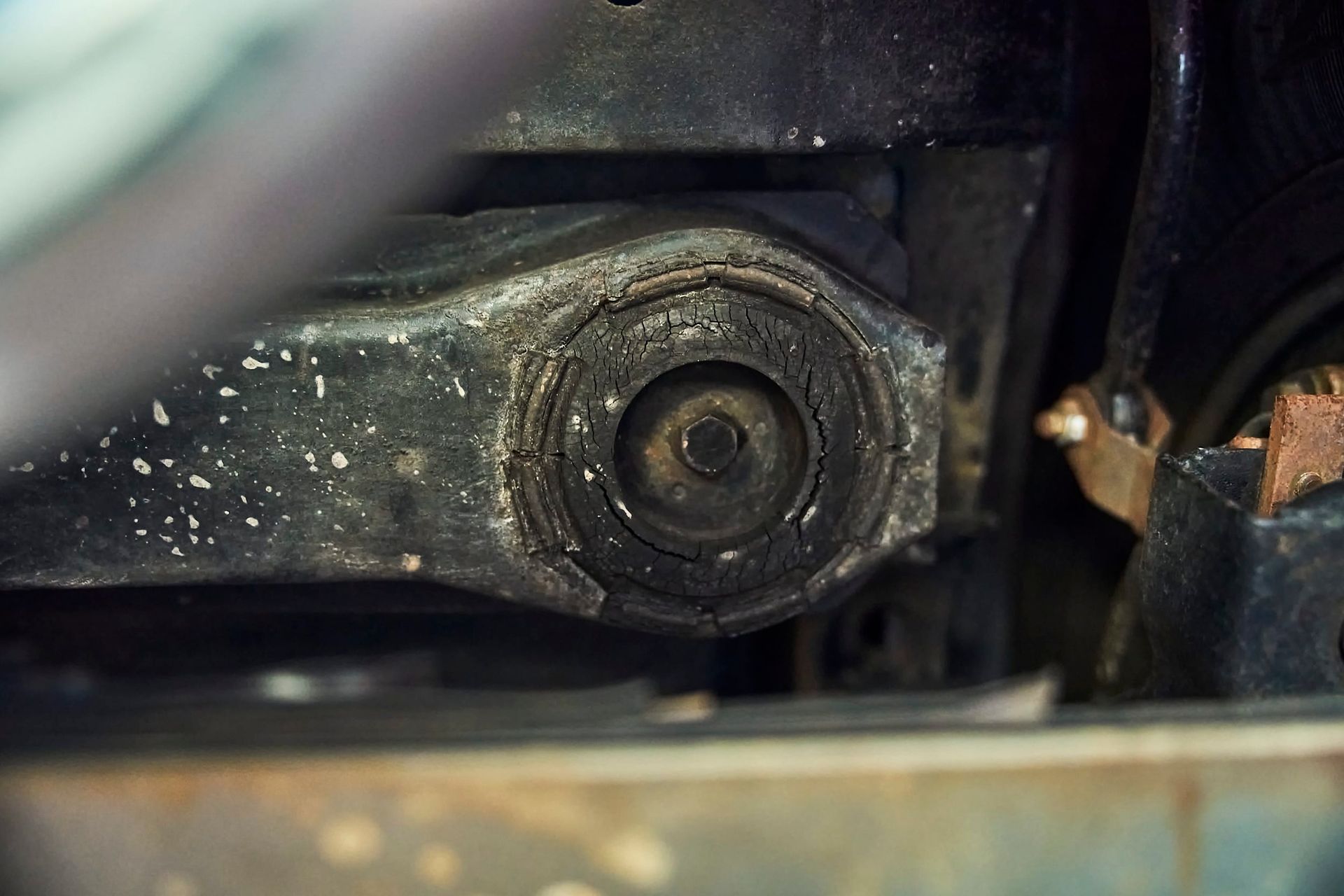 Close-up view of a black car suspension component, possibly a bushing, with visible wear and cracking.