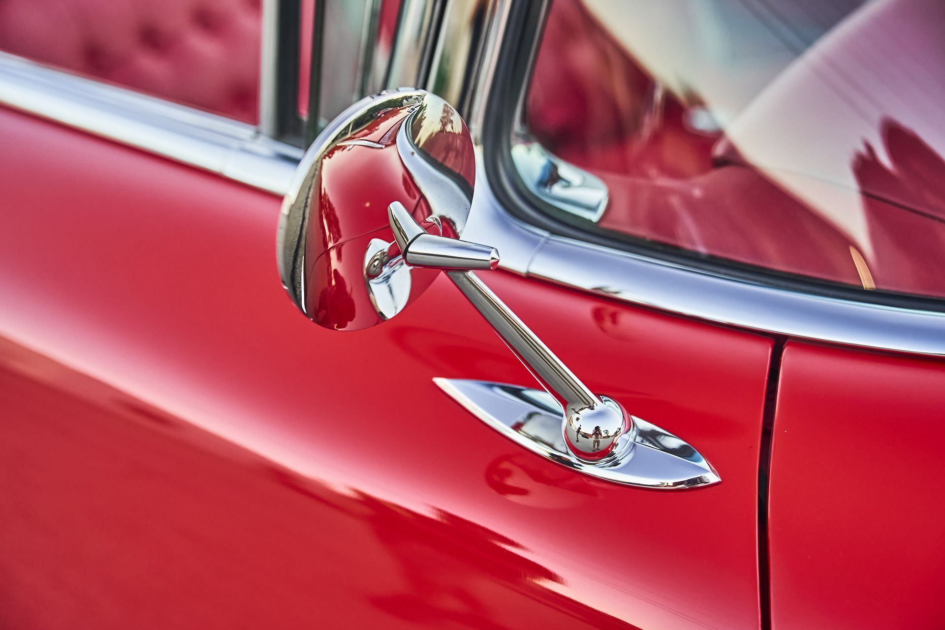 A close up of a red car with a chrome side mirror.