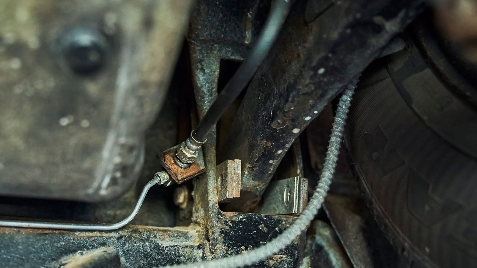 Close-up of a vehicle's undercarriage with a black cable connected to a rusty metal fitting, fastened to a black beam.