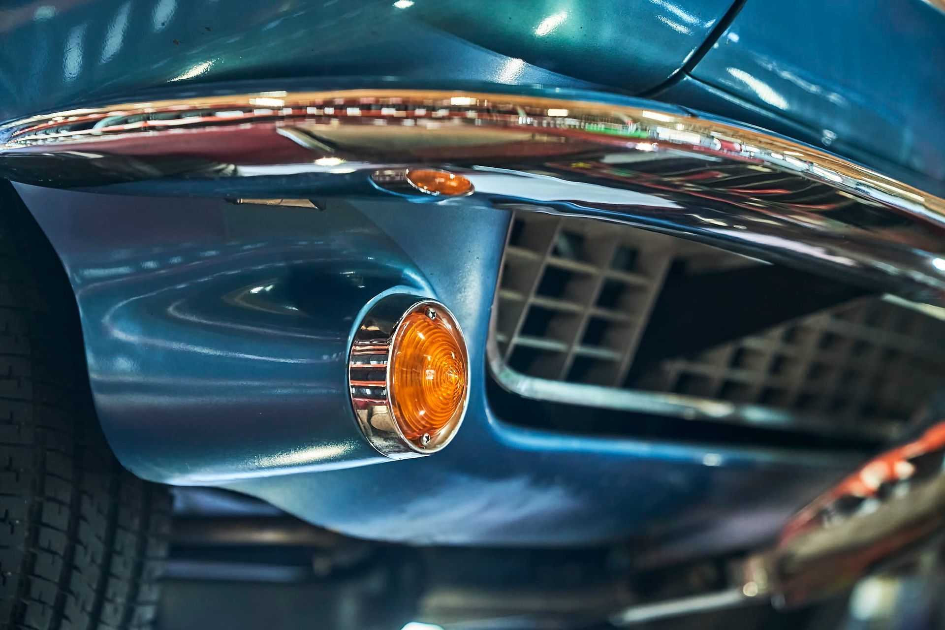 Close-up of a teal vintage car's front bumper, featuring chrome trim and an orange turn signal light.