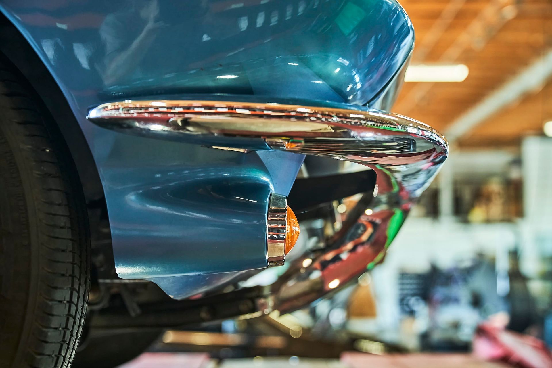 Close-up of a teal vintage car's front bumper with chrome detailing and an orange light.