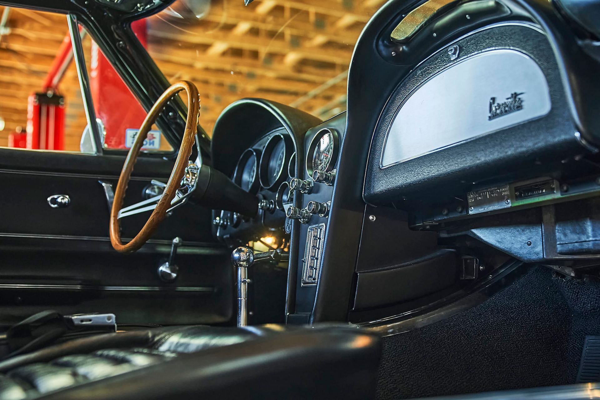 Interior of a black vintage Corvette. Wooden steering wheel, gauges, and gear shift are visible.