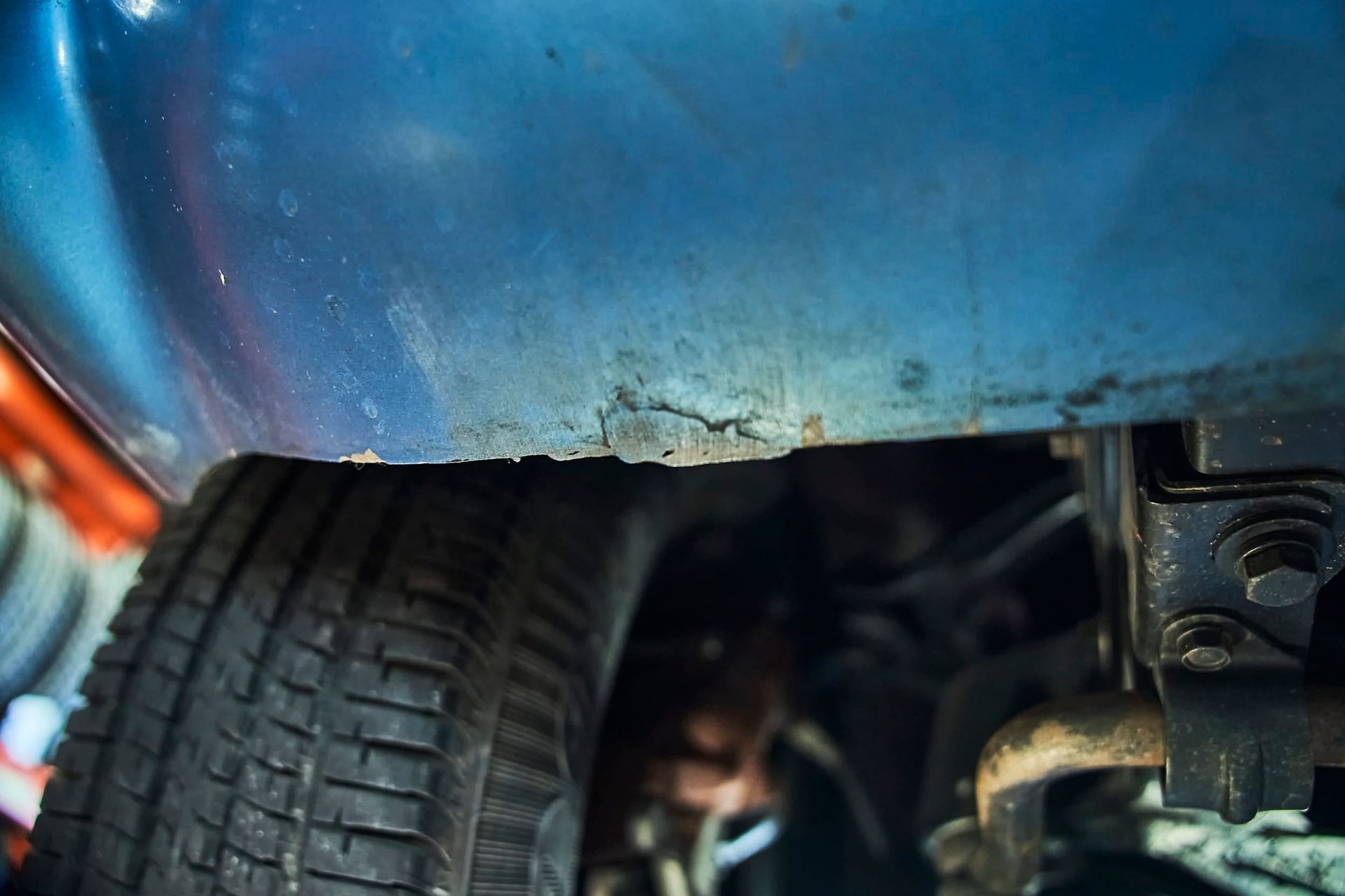 Blue car's rusted rocker panel above a tire. The rust exposes metal.
