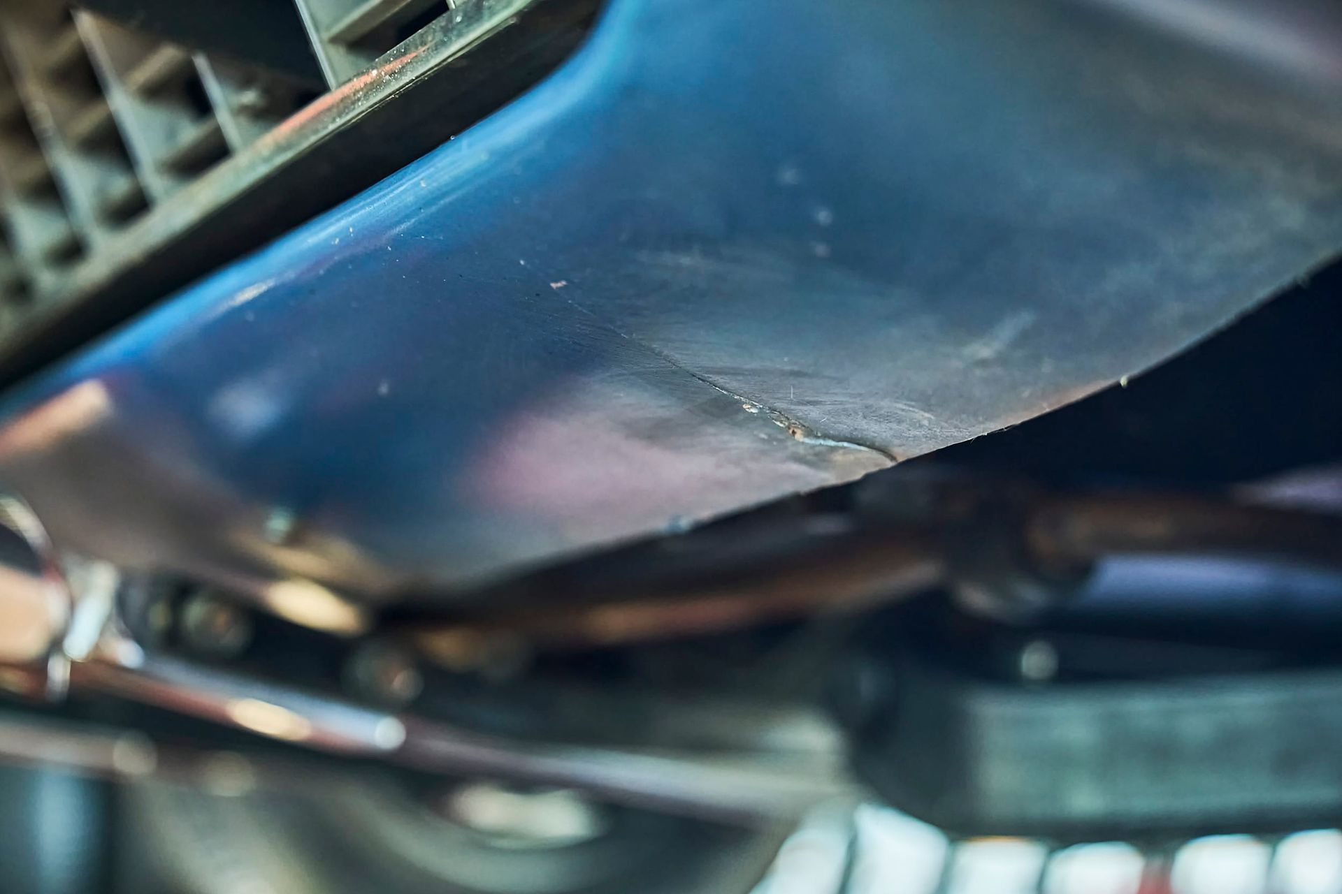 Close-up view of a blue car undercarriage, revealing a crack along a curved, textured surface.