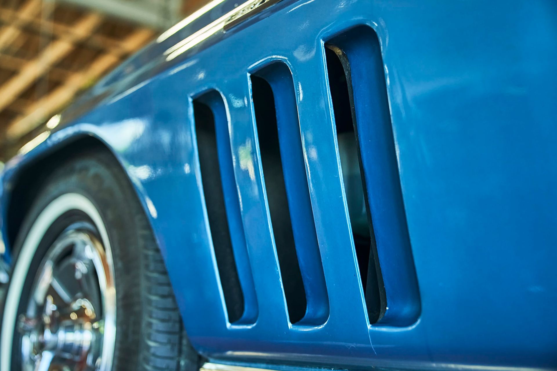 Blue classic car side with vertical air vents near the wheel. The tire has a white wall.