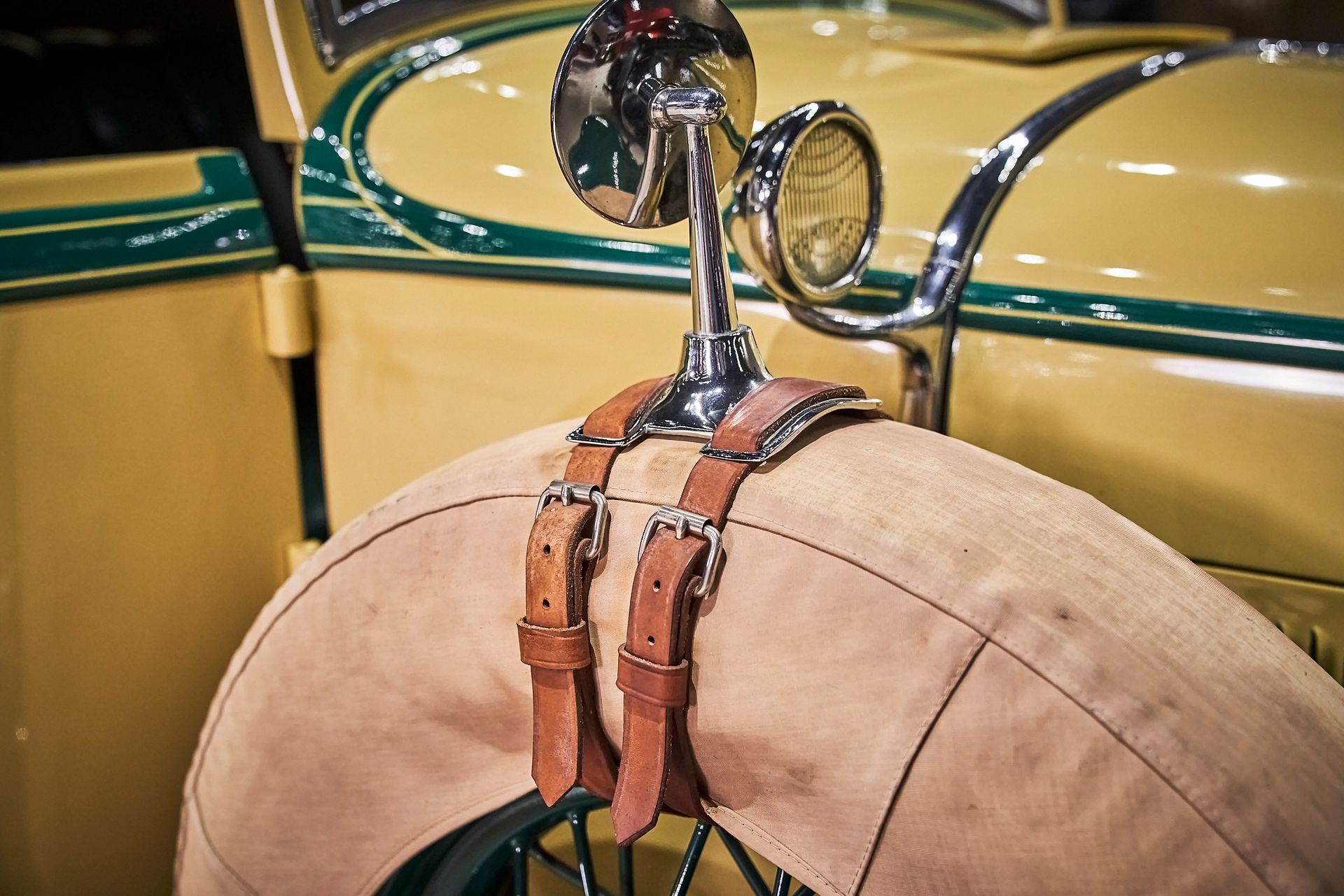 A close up of a tire on an old car with leather straps attached to it.