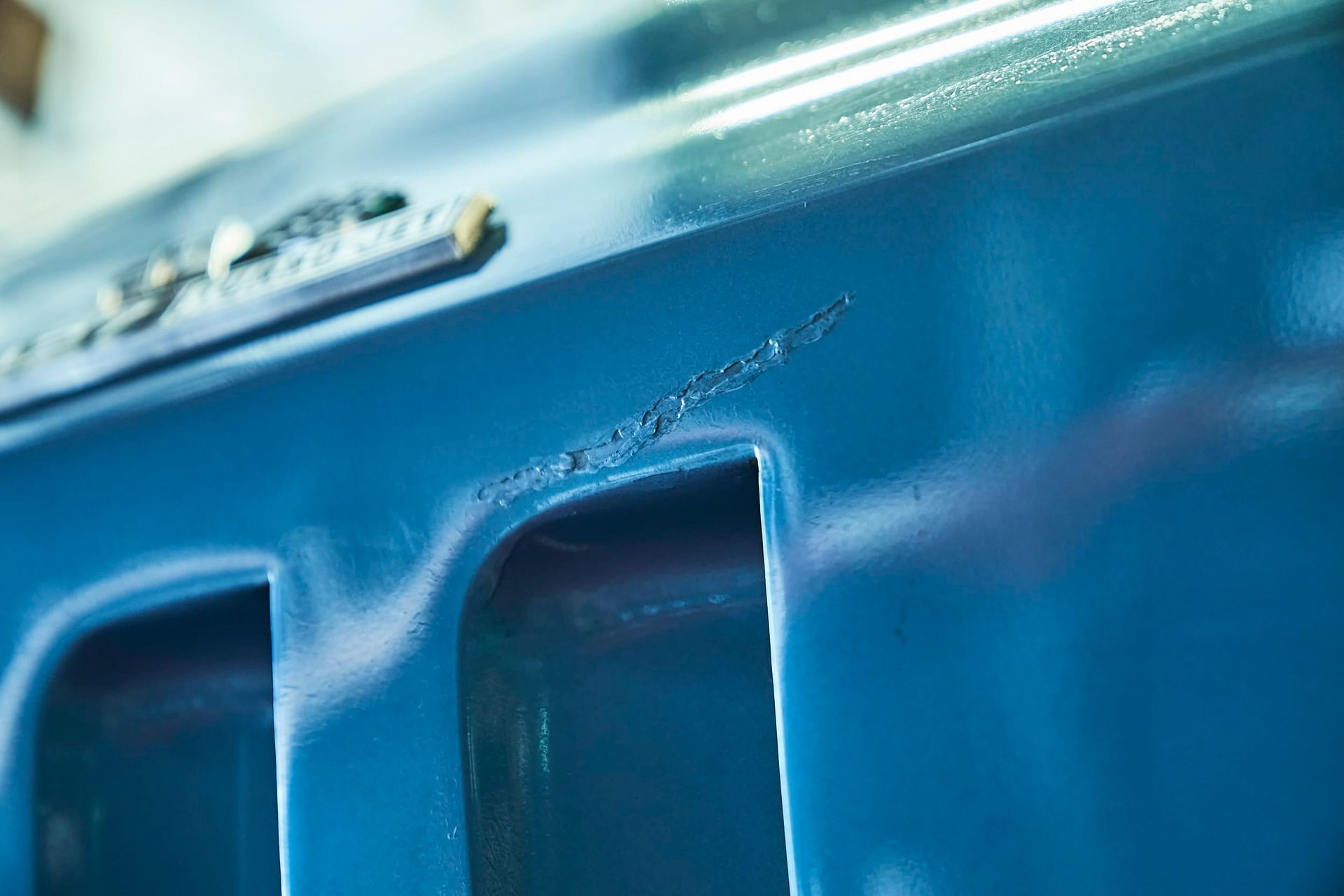 Close-up of a blue car part with a scratch or gouge.