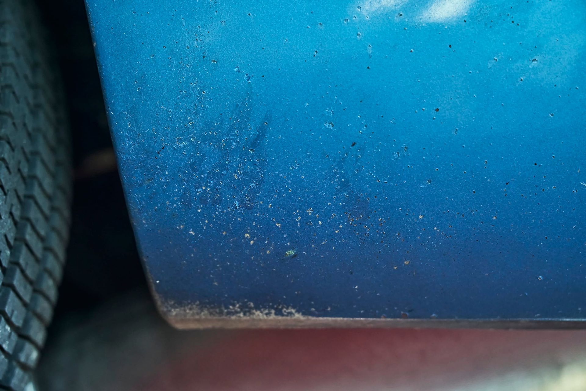 Close-up of a blue car door with visible paint imperfections and a tire in the left corner.