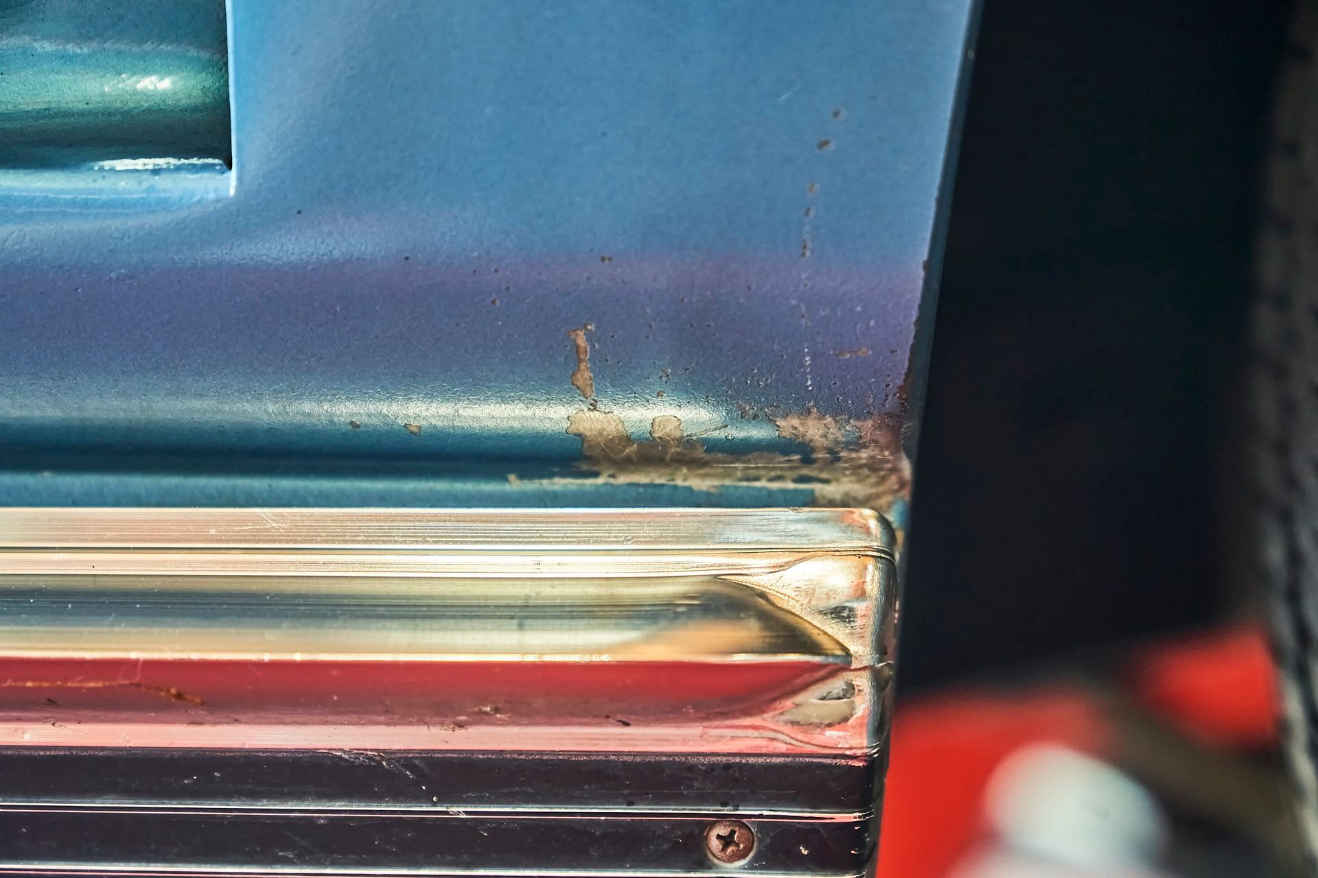 Rust spots on a blue car door's edge with chrome trim, showing signs of aging and potential damage.