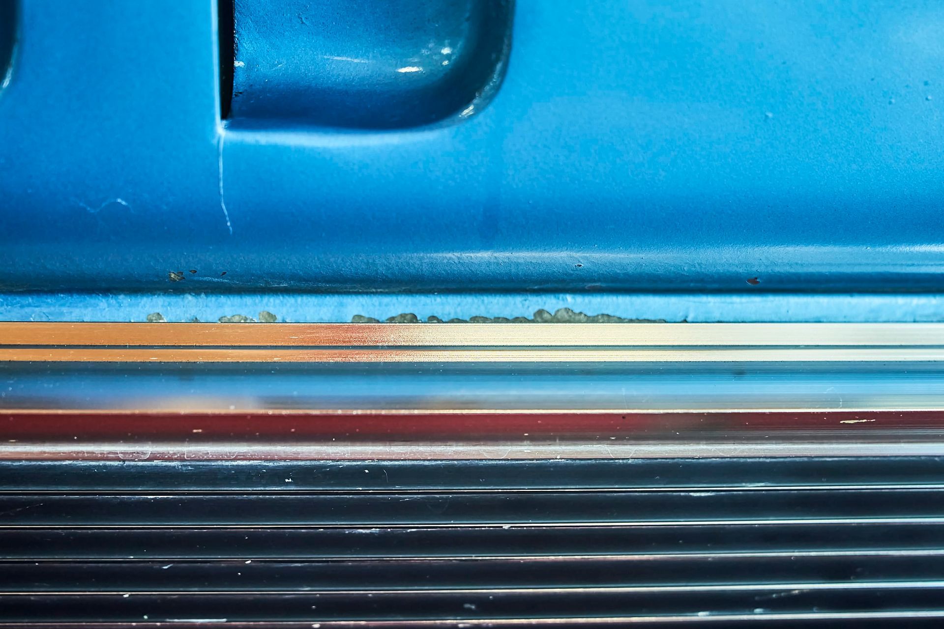 Close-up view of blue car body with rust spots on a horizontal trim piece.
