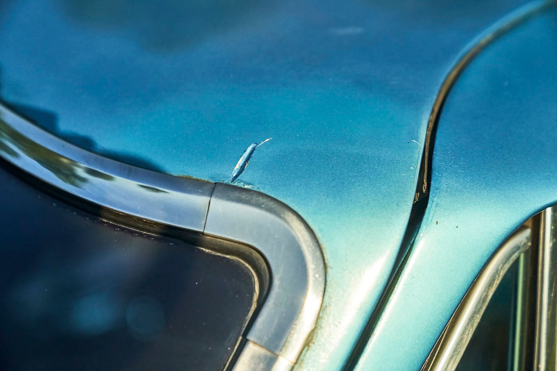 Close-up of a vintage teal car's body with a chrome trim, showing a small scratch.