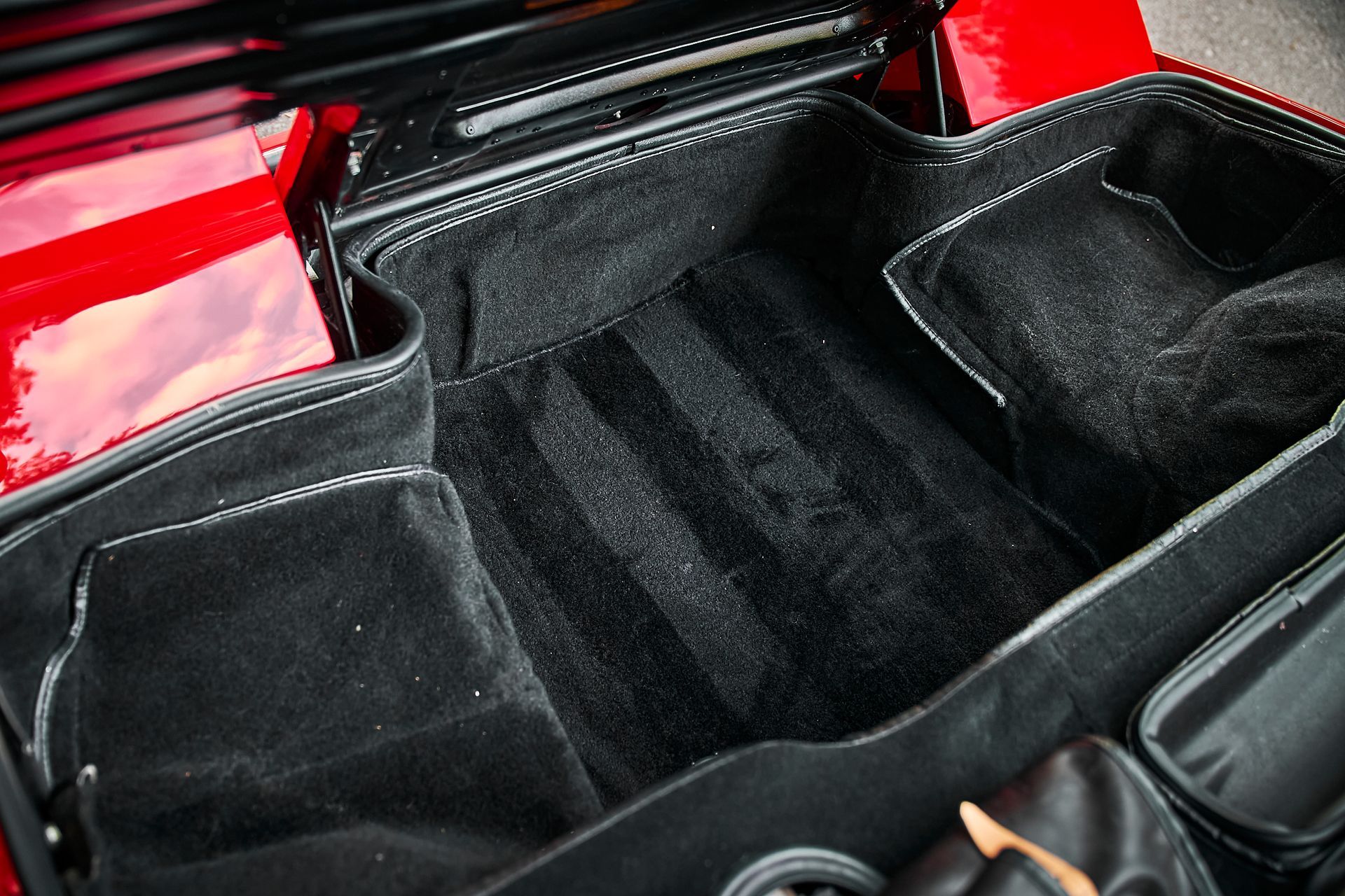The trunk of a red car with a black bag in it.