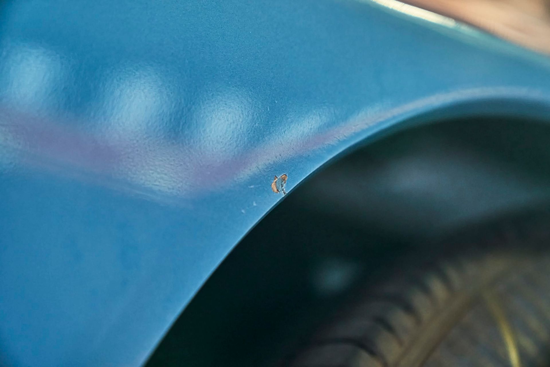 Close-up of a blue car fender with a small spot of rust near a tire.