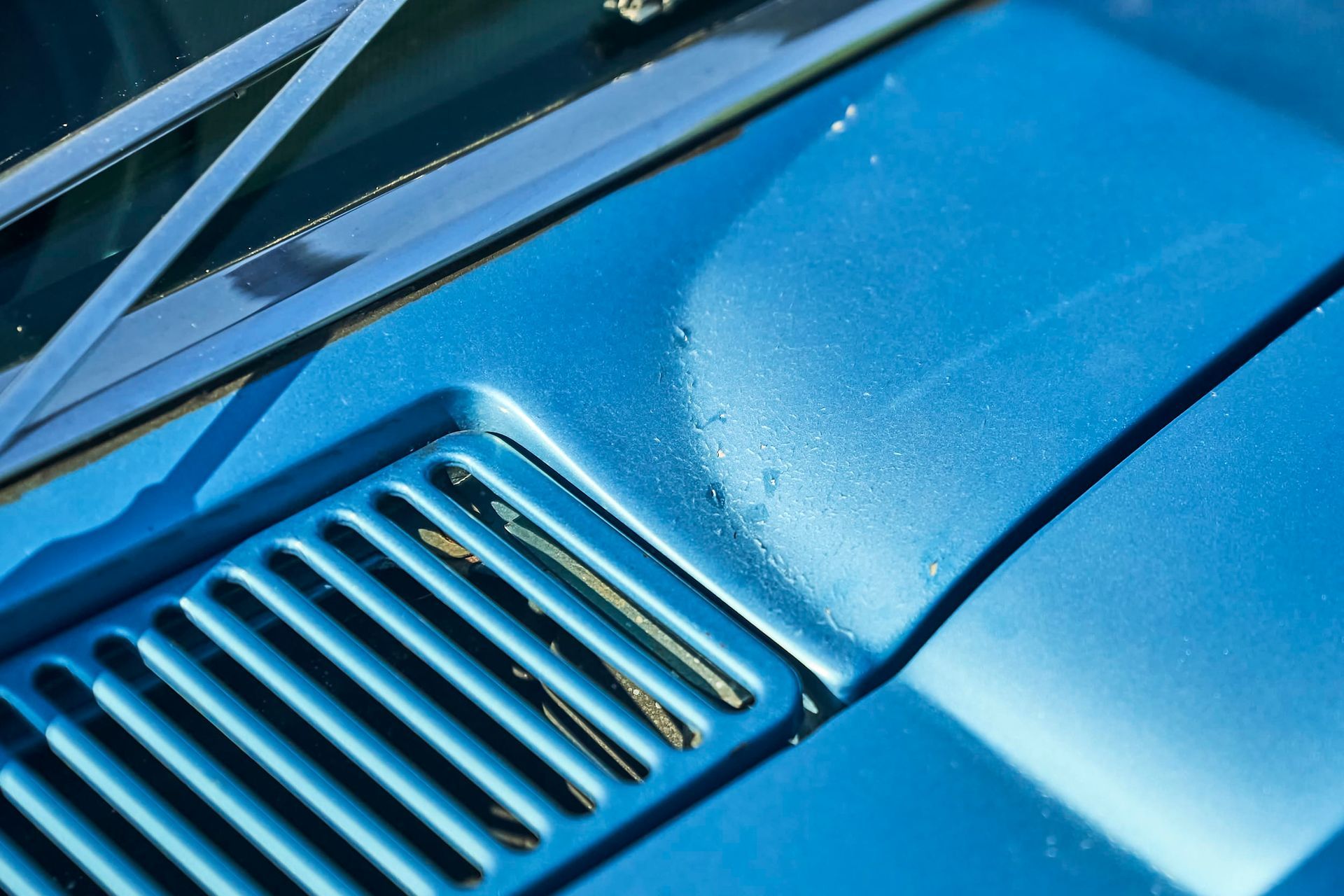 Close-up of a bright blue car hood with a vent, windshield wiper, and water droplets.