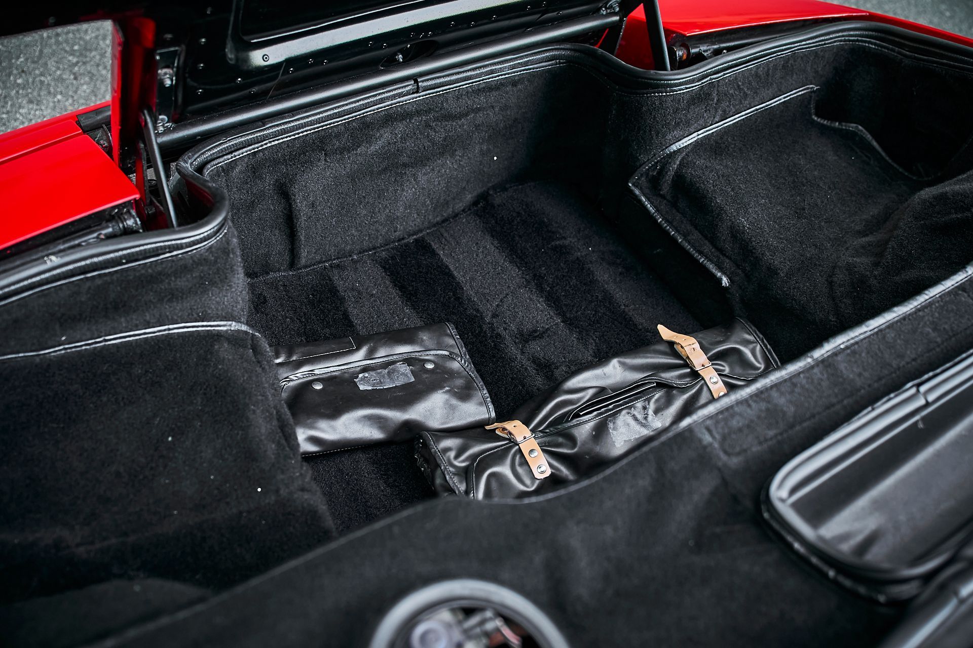 The trunk of a red car with a black bag in it.