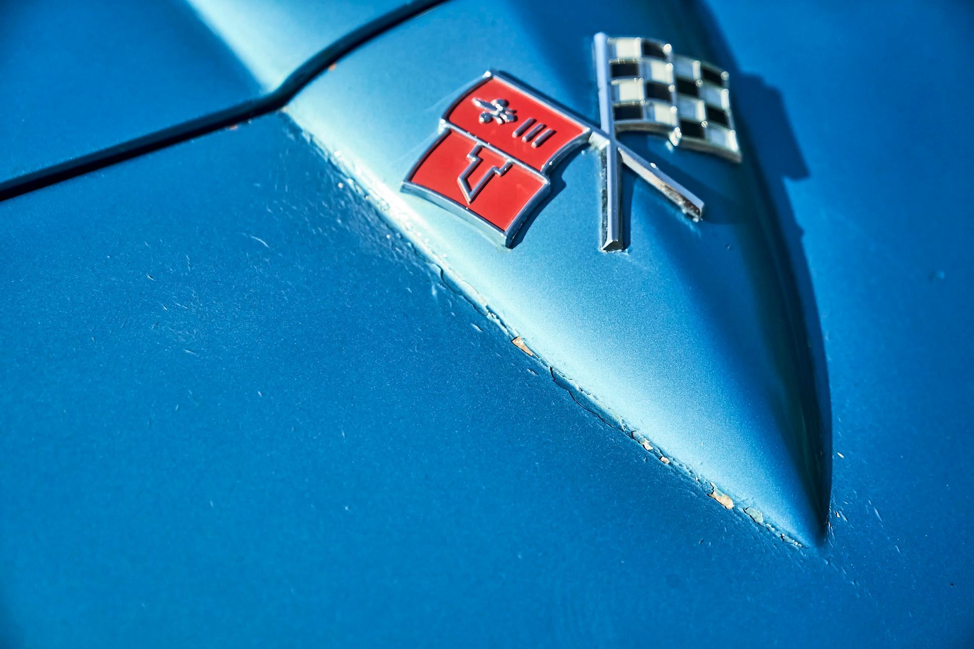 Close-up of a blue car hood with a red flag emblem and a checkered flag emblem.